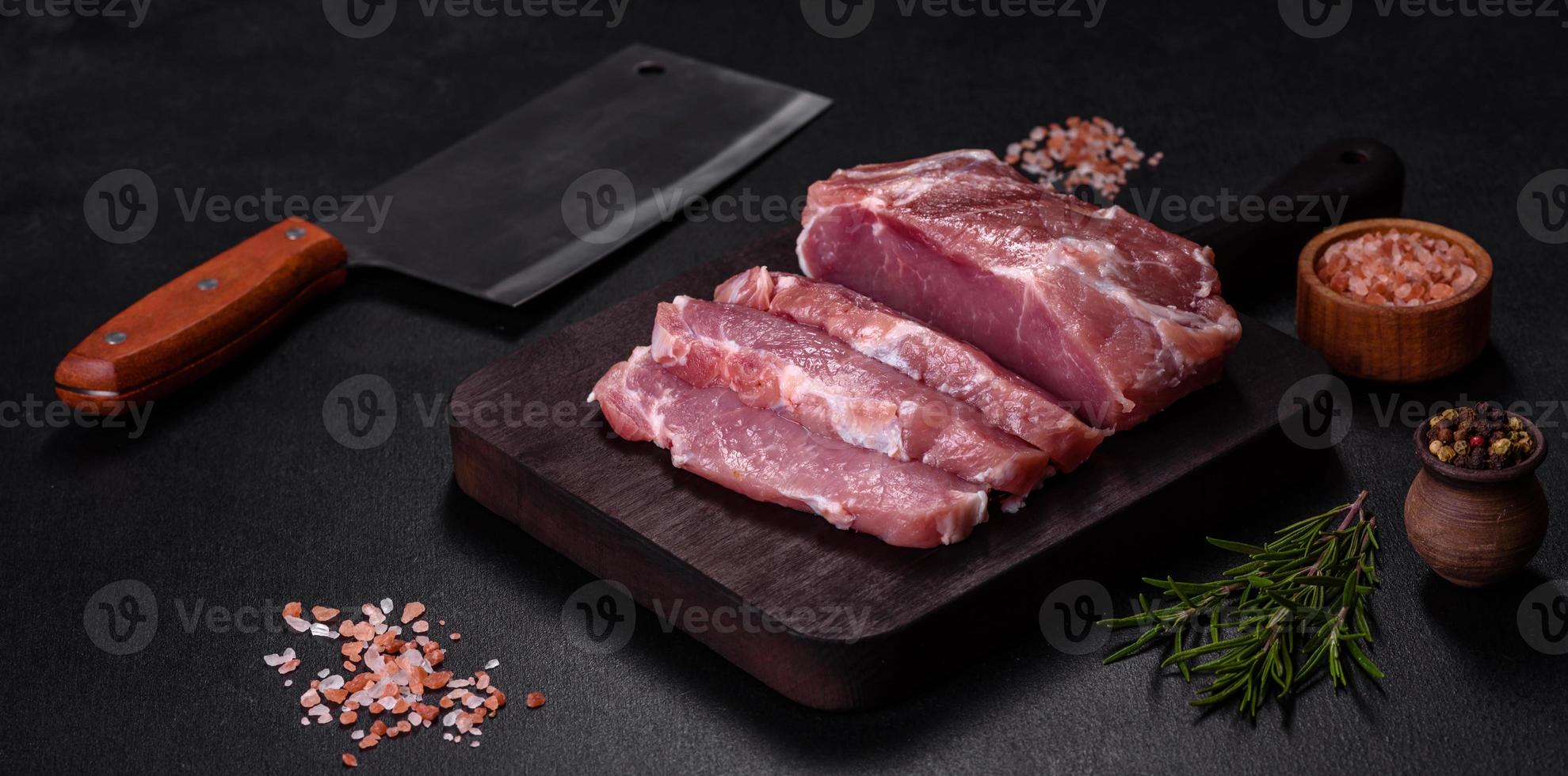 frisches Stück rohes Schweinefleisch mit Gewürzen, Salz und Kräutern auf einem Holzschneidebrett foto