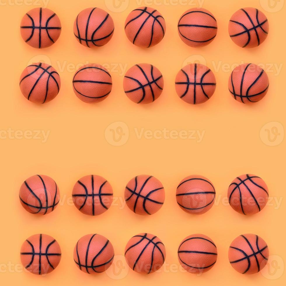 Viele kleine orangefarbene Bälle für Basketball-Sportspiele liegen auf Texturhintergrund aus modepastellorangefarbenem Papier in minimalem Konzept foto