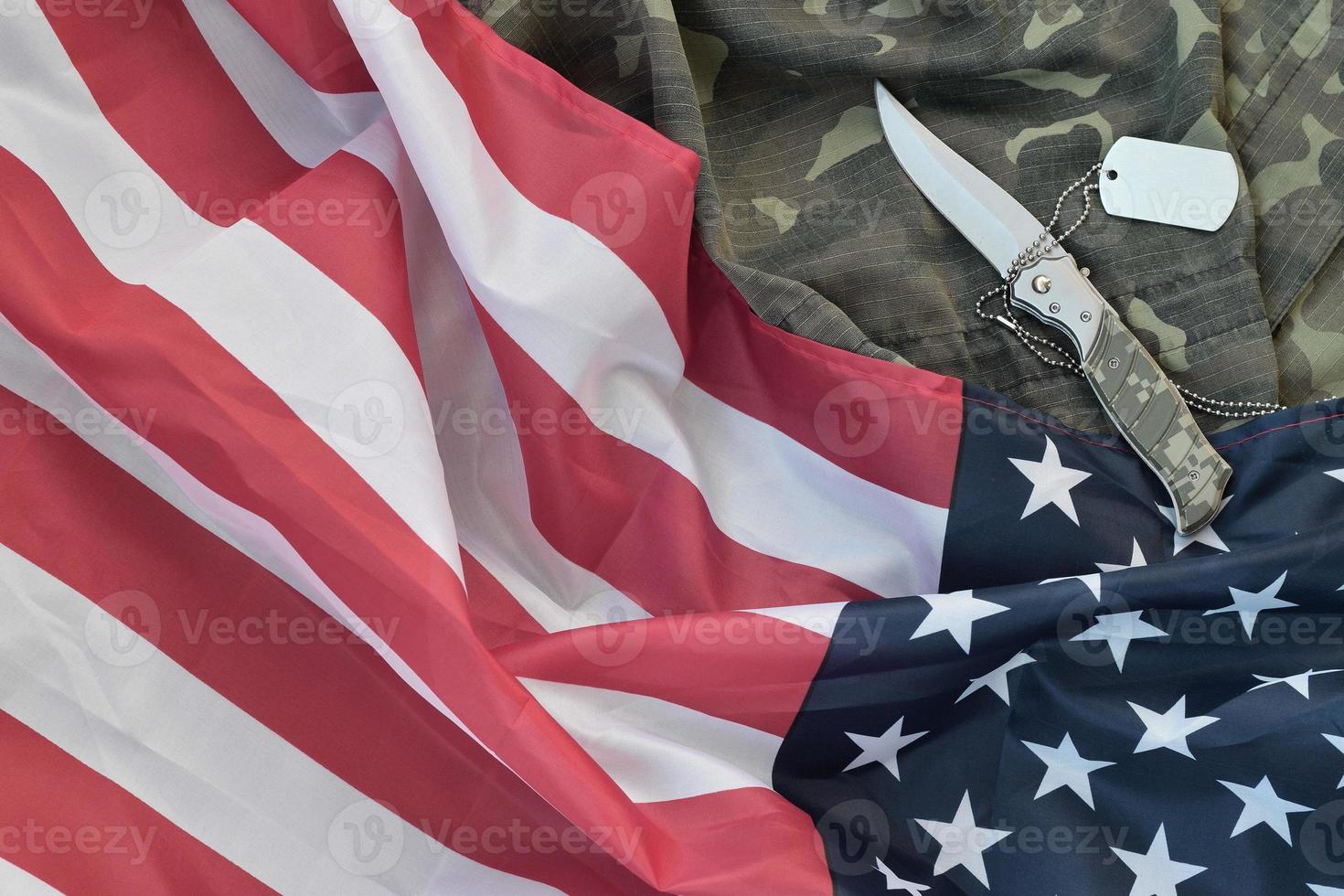 Army Dog Tag Token und Messer liegen auf alter Tarnuniform und gefalteter Flagge der Vereinigten Staaten foto