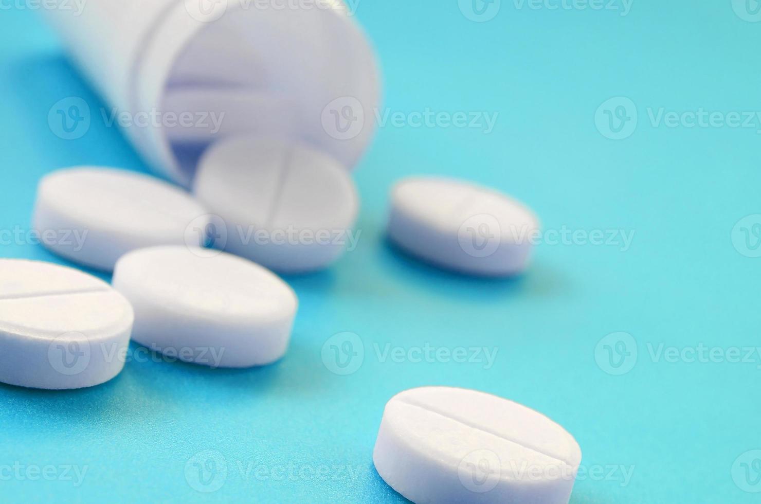 mehrere weiße tabletten fallen aus dem plastikglas auf die blaue oberfläche. Hintergrundbild zu medizinischen und pharmazeutischen Themen foto