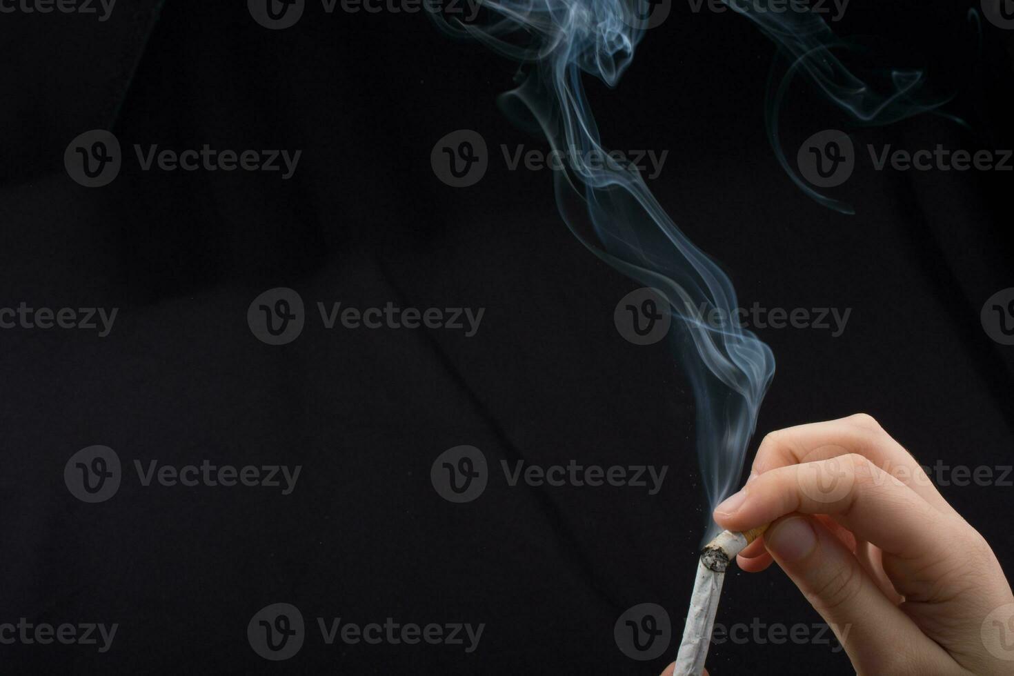 Hand hält rauchende Zigarette auf schwarzem Hintergrund foto