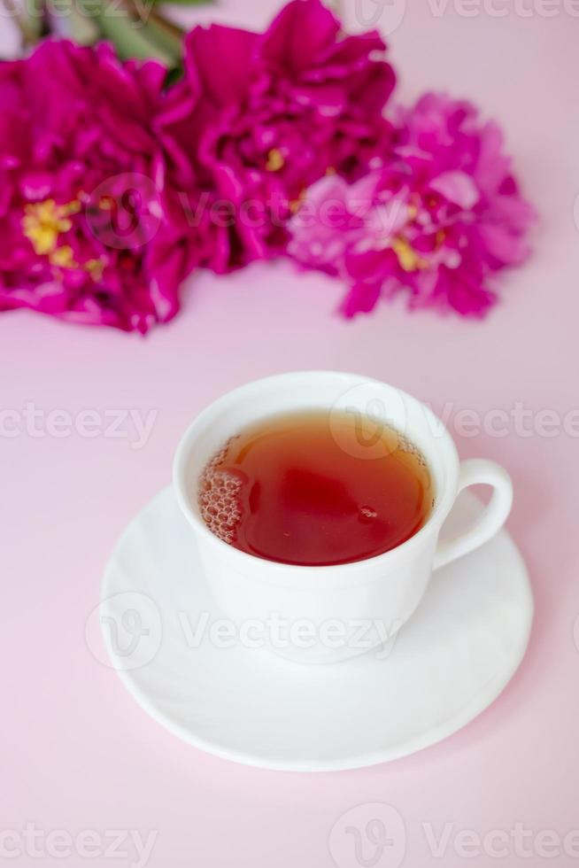 eine tasse tee vor dem hintergrund eines üppigen blumenstraußes aus burgunderfarbenen pfingstrosen, nahaufnahme auf einem rosa hintergrund foto