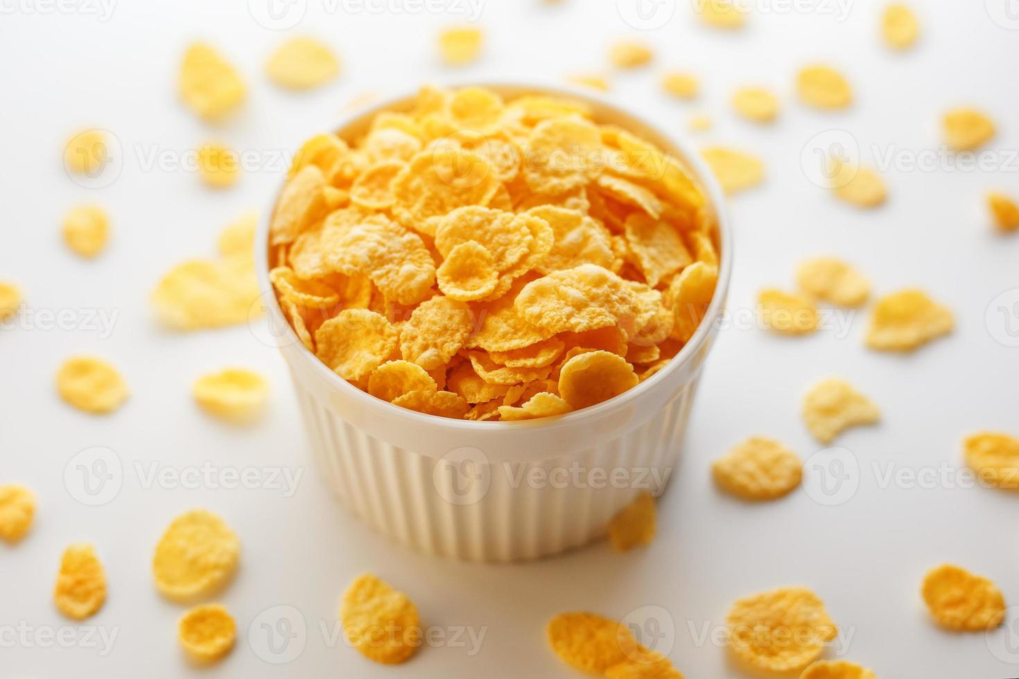 weiße Tasse mit goldenen Cornflakes, isoliert auf weißem Hintergrund. Hopya zerbröckelte um die Tasse herum. Sicht von oben foto