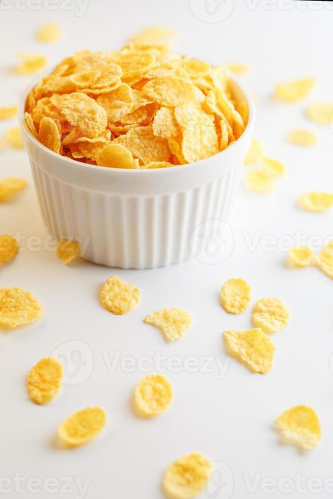 weiße Tasse mit goldenen Cornflakes, isoliert auf weißem Hintergrund. Hopya zerbröckelte um die Tasse herum. Sicht von oben foto