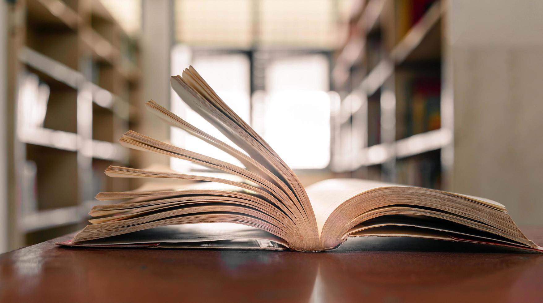 ein offenes buch oder lehrbuch in der bibliothek mit licht aus dem fenster auf dem lesetisch und dem korridor der bücherregale im schulklassenzimmerhintergrund. bildungslernkonzept foto