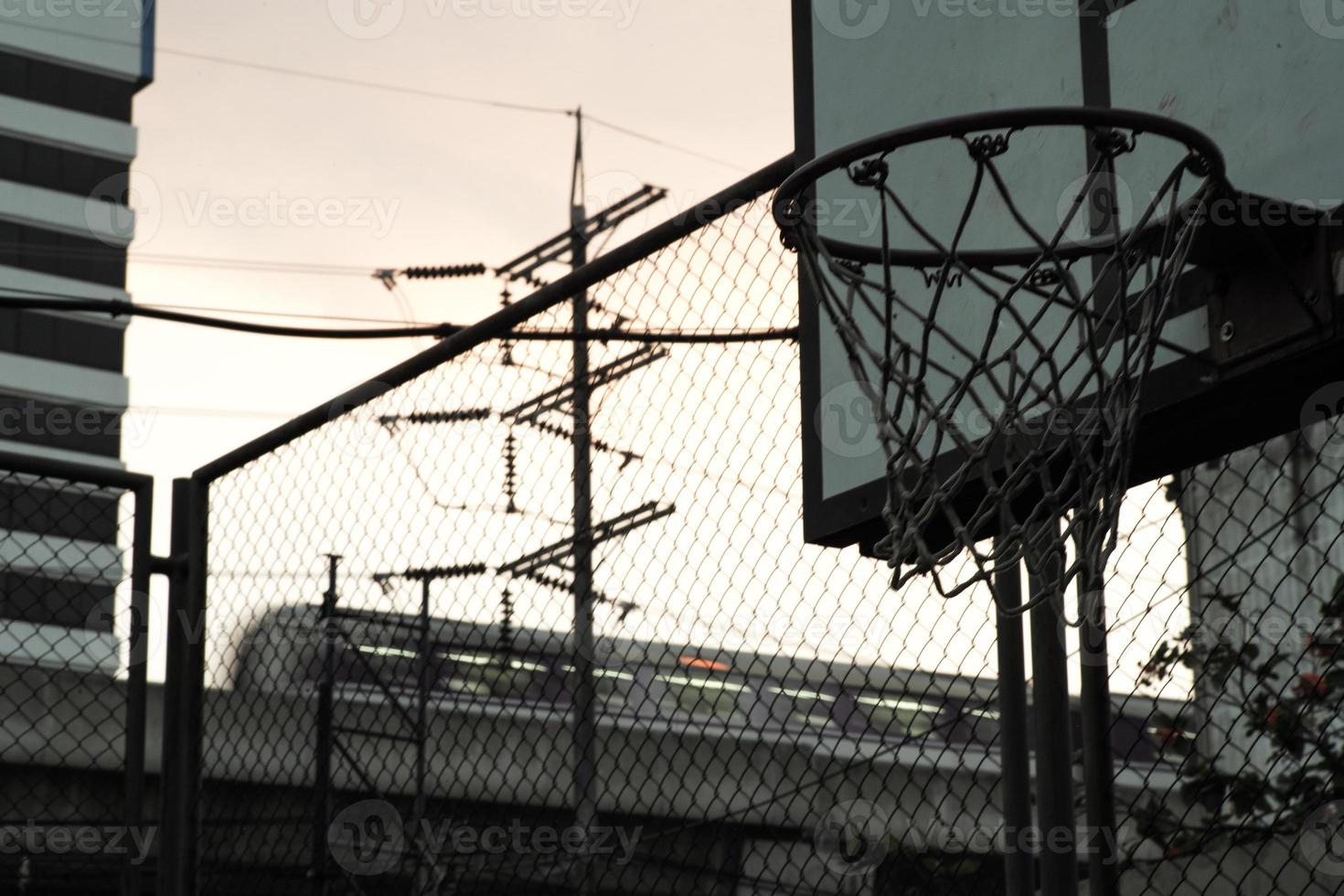 Blick aus der Vogelperspektive auf den alten Basketballkorb mit bewegungsunscharfem Zug im Hintergrund des Dämmerungshimmels foto