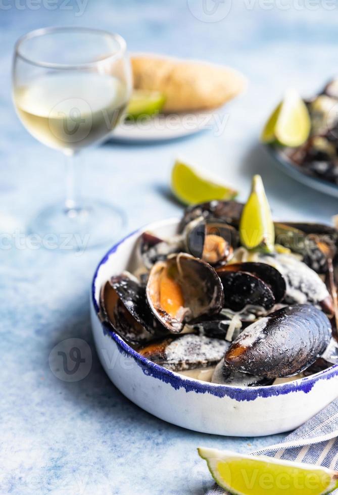 Miesmuscheln in cremiger Weißweinsauce, serviert mit Limette und Brot. Muscheln in Wein, Lauch und Blauschimmelkäse schmoren. Meeresfrüchte. foto