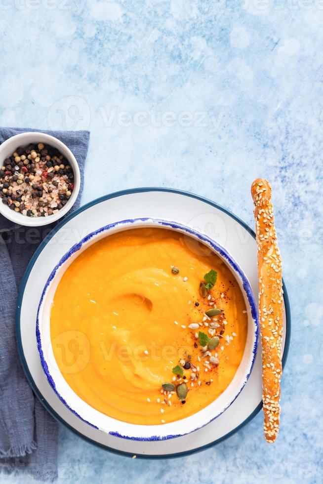 Helle vegetarische Herbstkürbis- und Karottensuppe mit Samen, Minze und Gewürzen, blauer Hintergrund. Hausmannskost, gesundes Slow-Food-Konzept für Herbst und Winter. foto