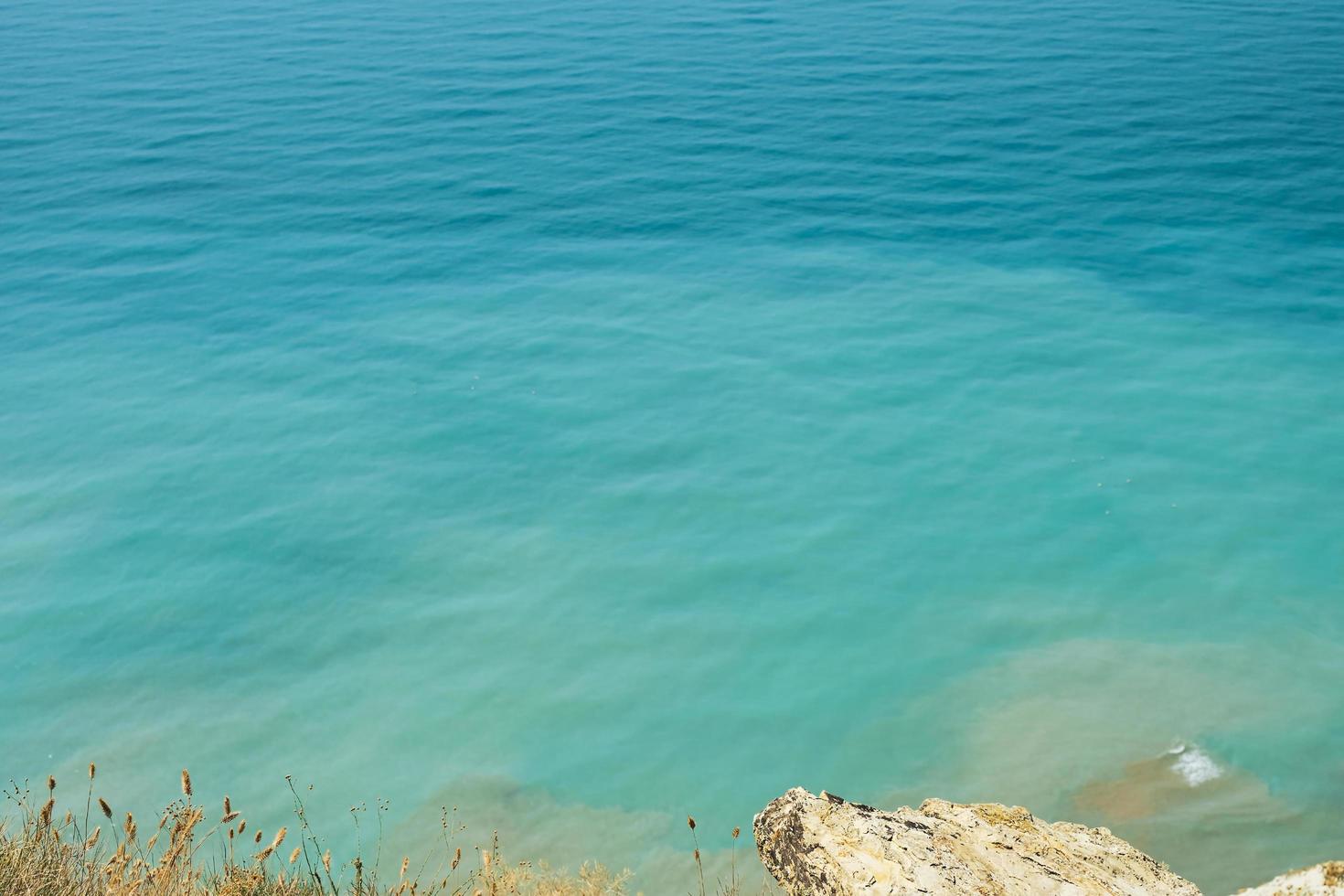 unscharfer Hintergrund, Blick auf das Meer in der Mittagshitze vom felsigen Ufer. heiße sommerferien, pastellfarben und reflexionen auf dem wasser. abstraktes unschärfeplakat oder werbebanner foto