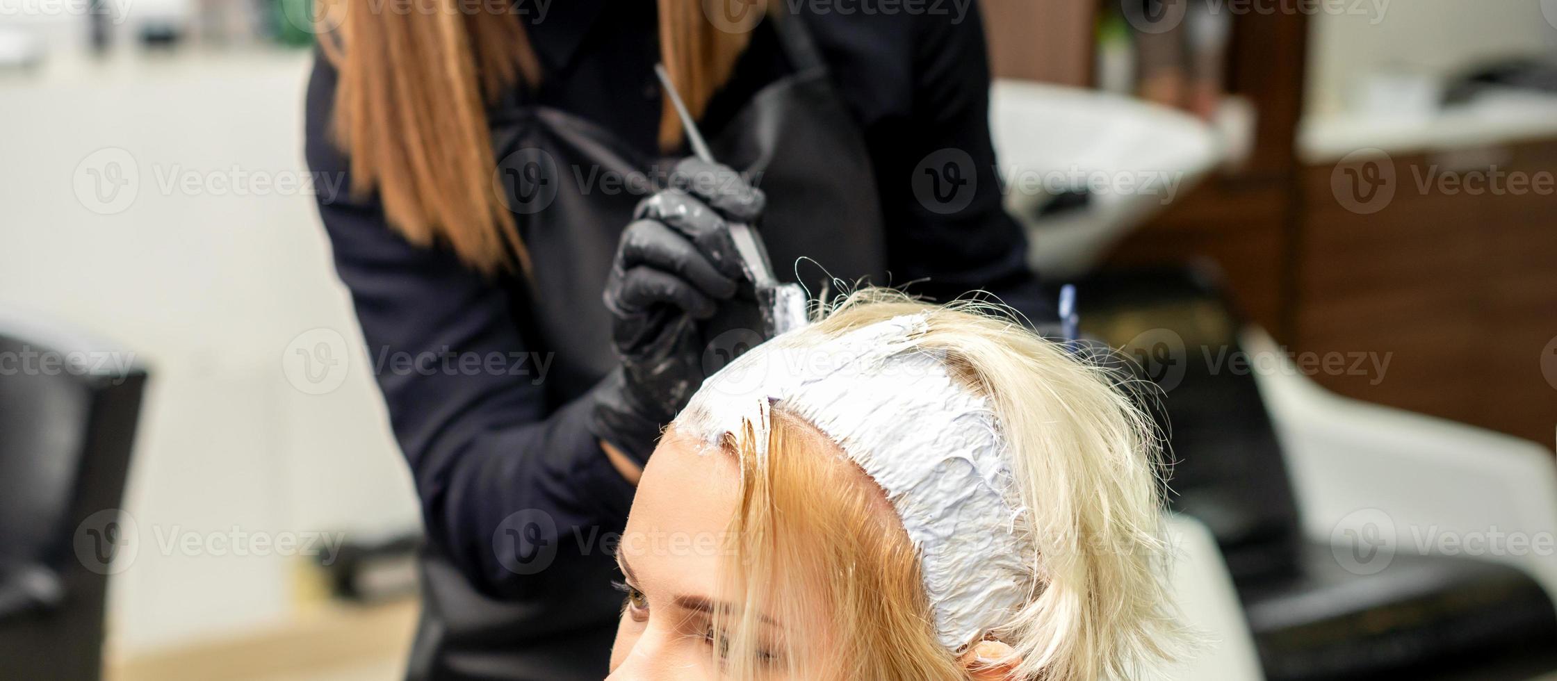 Der Stylist trägt weiße Farbe auf das Haar auf foto