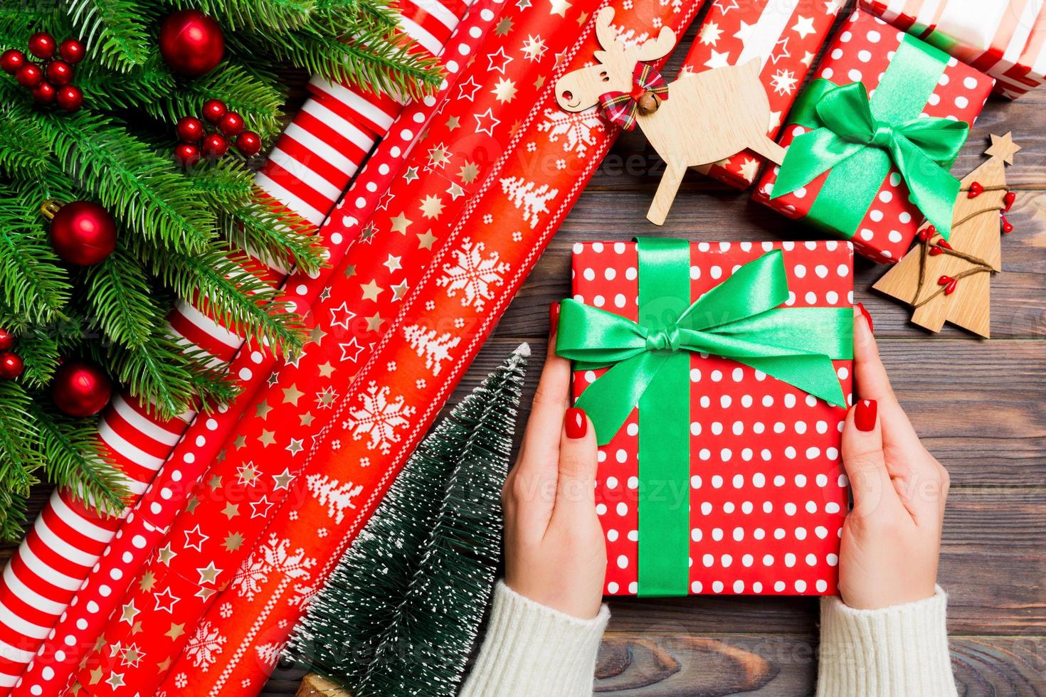 Draufsicht einer Frau, die eine Geschenkbox in ihren Händen auf festlichem hölzernem Hintergrund hält. Tannenbaum und Weihnachtsschmuck. neujahrszeitkonzept foto