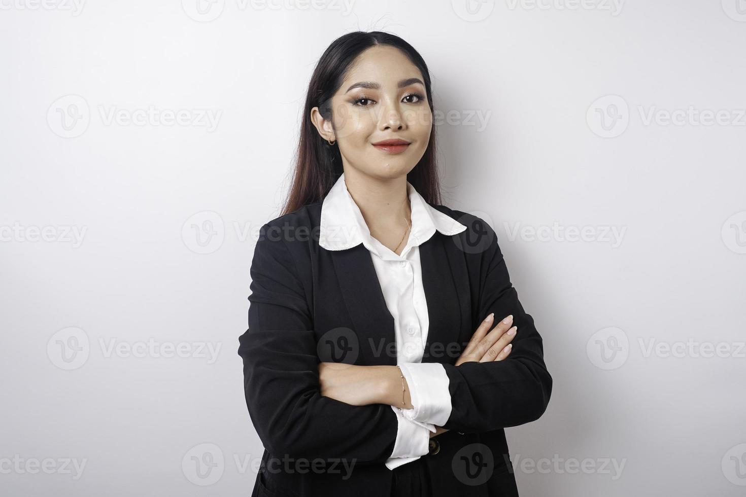 Porträt einer selbstbewusst lächelnden asiatischen Chefin mit schwarzem Anzug, die mit verschränkten Armen steht und isoliert auf weißem Hintergrund in die Kamera schaut foto