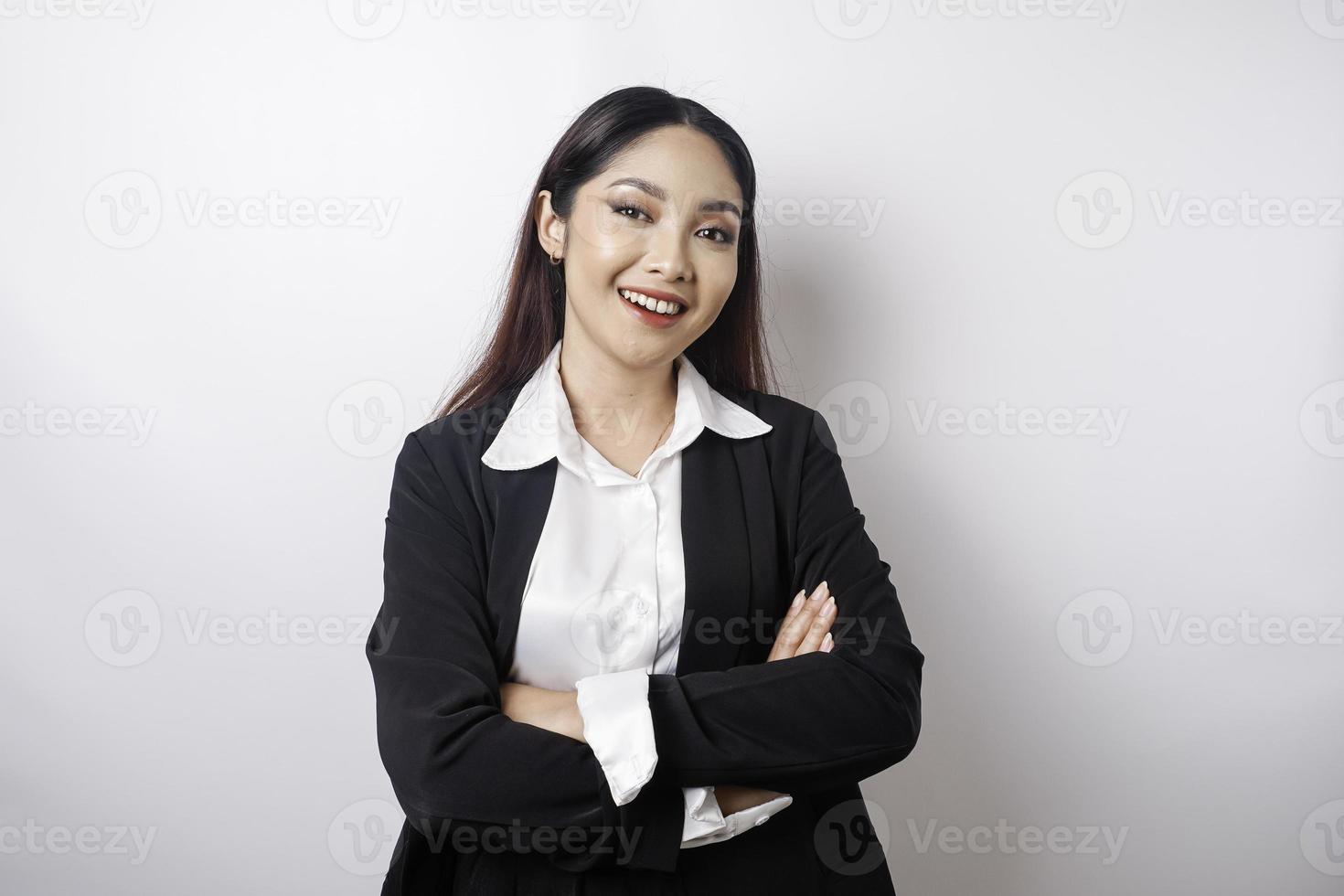 Porträt einer selbstbewusst lächelnden asiatischen Chefin mit schwarzem Anzug, die mit verschränkten Armen steht und isoliert auf weißem Hintergrund in die Kamera schaut foto