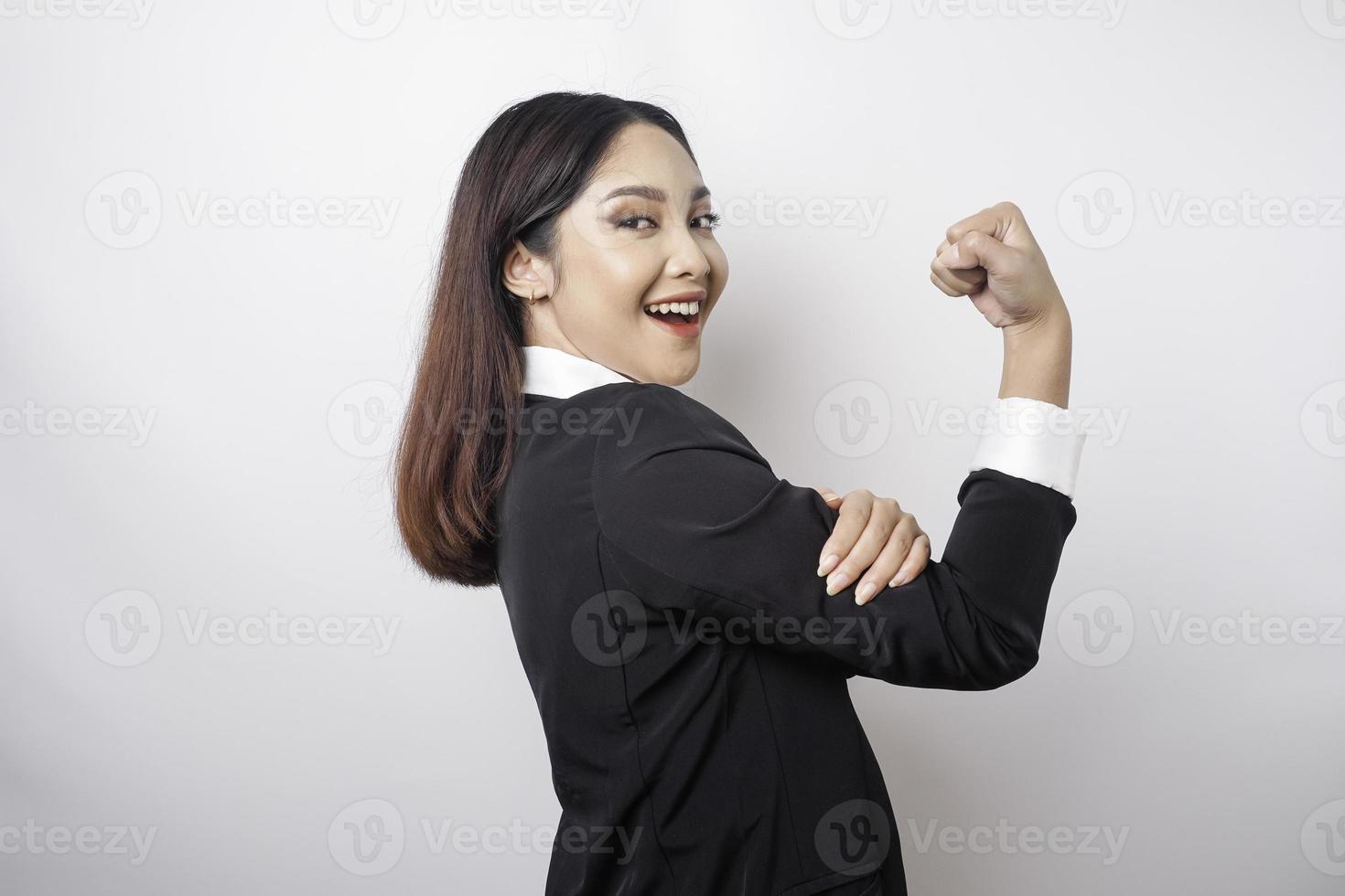 Aufgeregte asiatische Geschäftsfrau, die einen schwarzen Anzug trägt und eine starke Geste zeigt, indem sie ihre Arme und Muskeln stolz lächelt foto