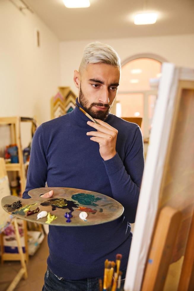 Der blonde Mann zeichnet ein Gemälde mit Öl foto