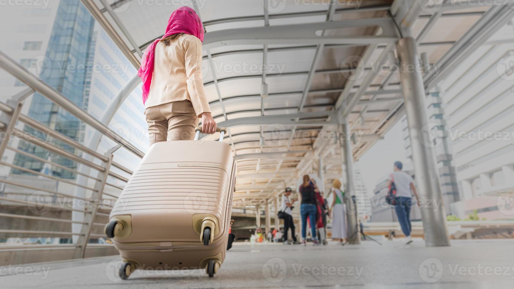 muslimische reisende frau, die einen koffer an einem reiseort im urlaub oder auf geschäftsreise geht und trägt, reisekonzepte, rückansicht. foto