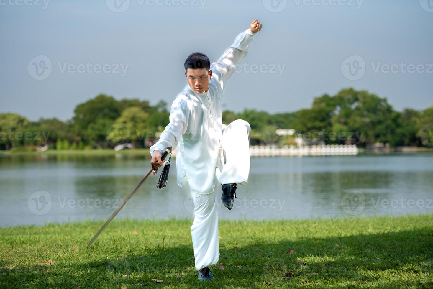 junger mann, der traditionelles tai chi-schwert, tai ji im park für gesundes, traditionelles chinesisches kampfkunstkonzept auf natürlichem hintergrund übt. foto