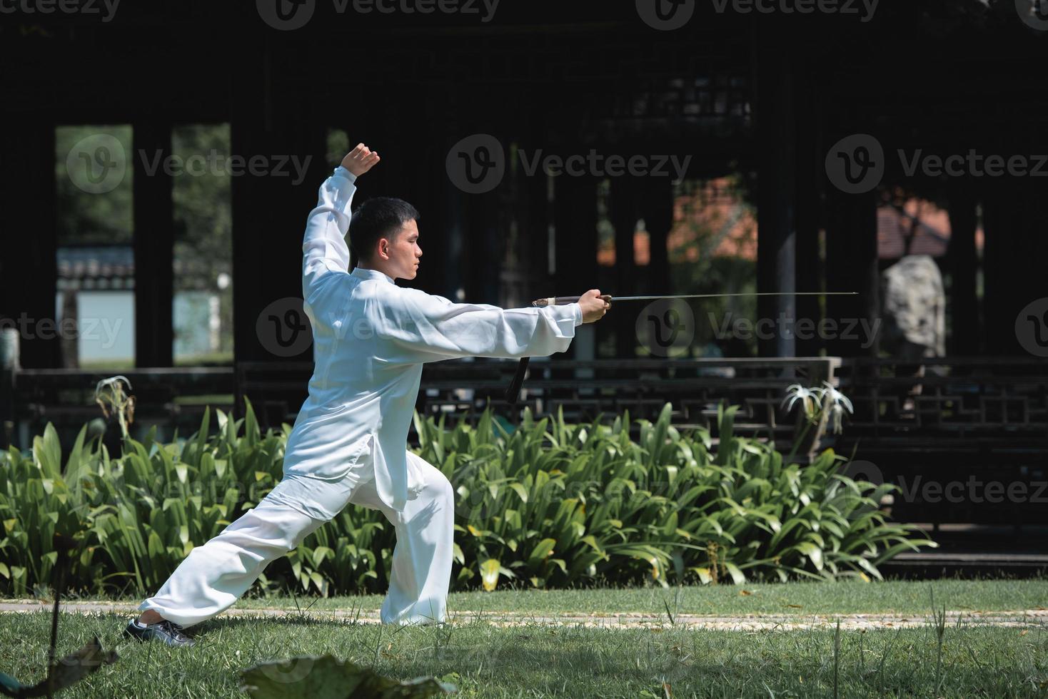 junger mann, der traditionelles tai chi-schwert, tai ji im park für gesundes, traditionelles chinesisches kampfkunstkonzept auf natürlichem hintergrund übt. foto