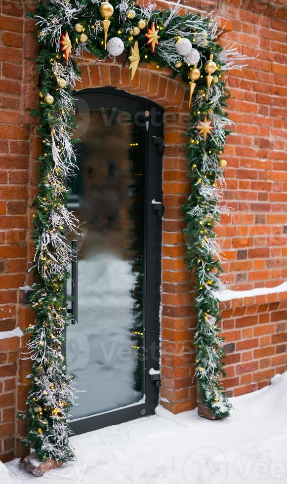 stilvolle weihnachts-tannenzweige mit kugeln und funkelnder girlande vor der tür auf dem feiertagsmarkt oder im restaurant in der stadtstraße. Winterweihnachtsstraßendekor foto