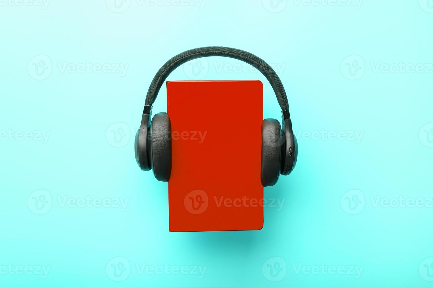 Kopfhörer werden auf einem Buch in einem roten Hardcover auf blauem Hintergrund getragen, Ansicht von oben. foto