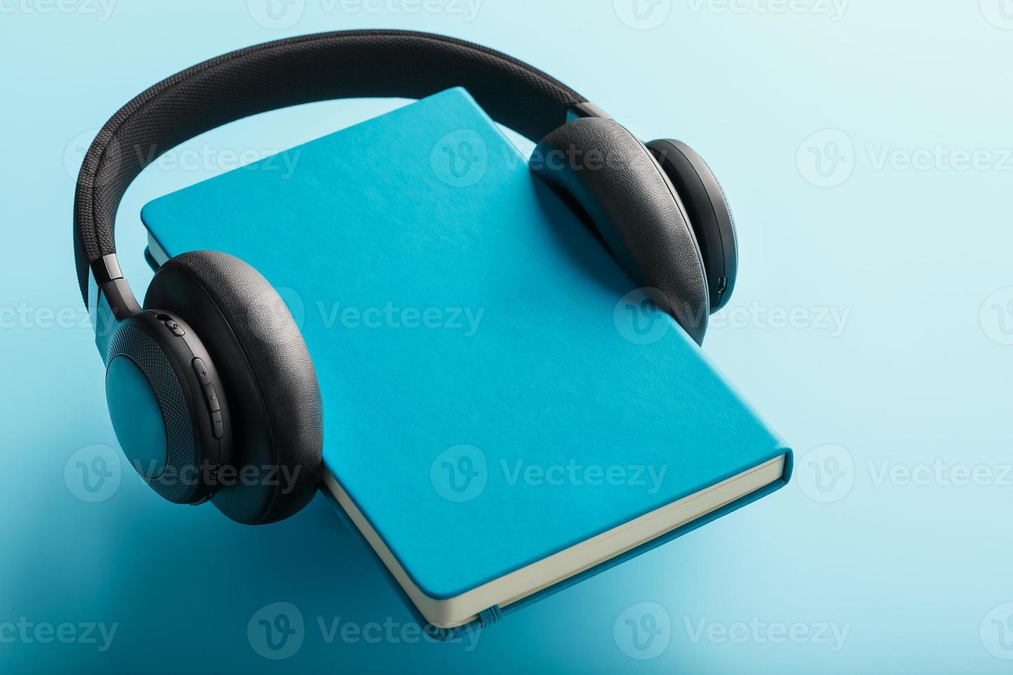 Kopfhörer werden auf einem Buch in einem blauen Hardcover auf blauem Hintergrund getragen, Ansicht von oben. foto