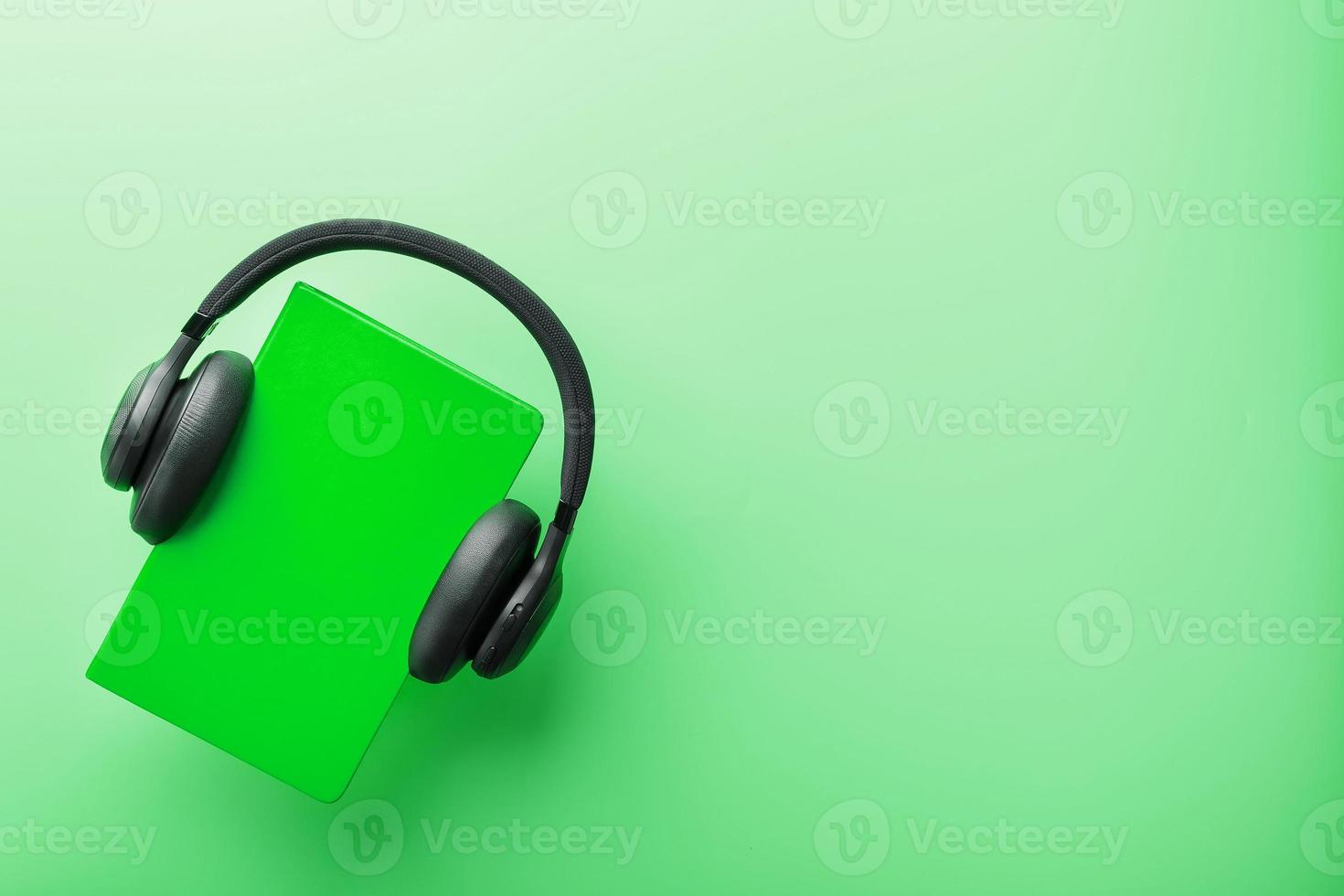 Kopfhörer werden auf einem Buch in einem grünen Hardcover auf grünem Hintergrund getragen, Ansicht von oben. foto