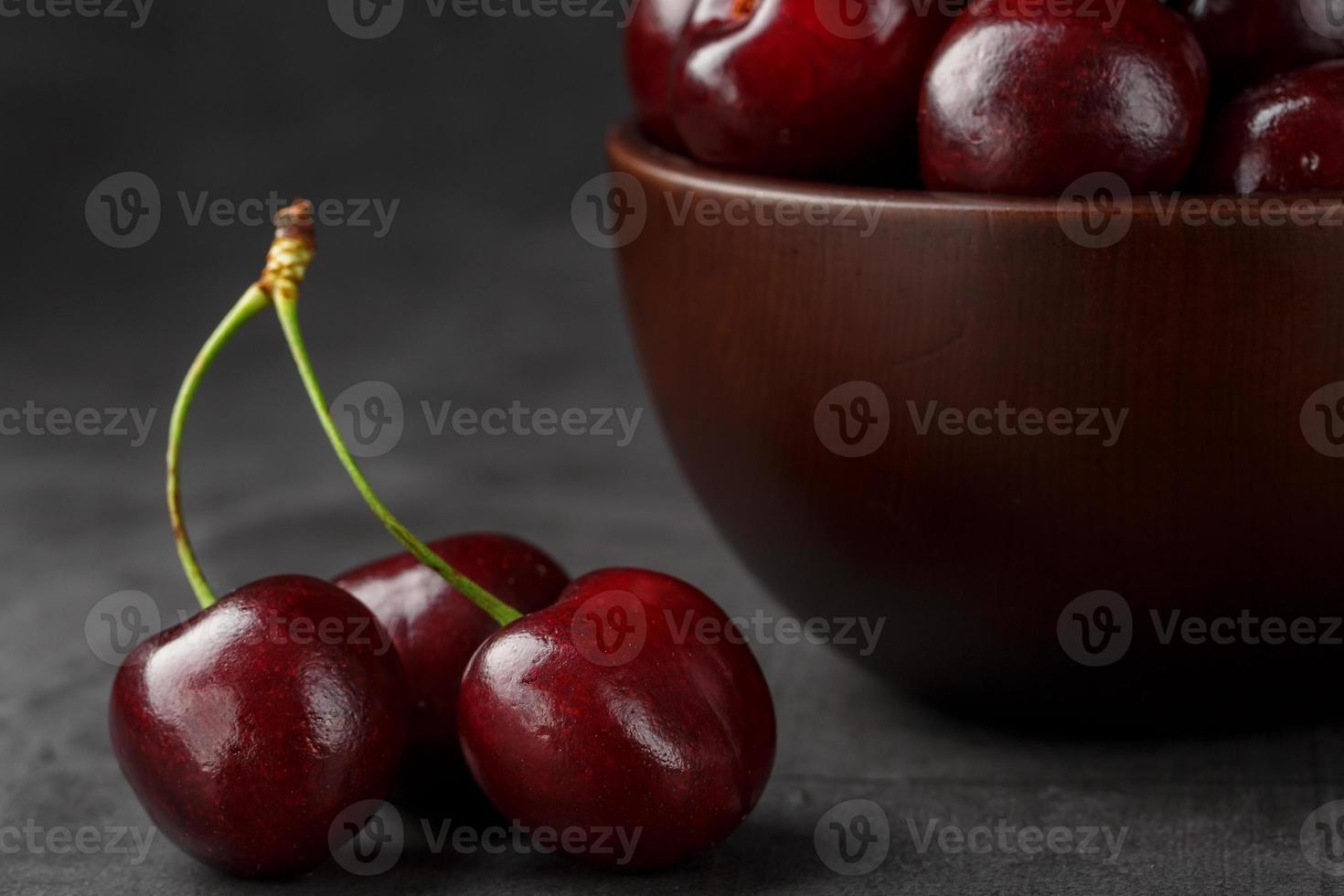 Reife und saftige Kirschbeeren auf einem schwarzen strukturierten Hintergrund in einer braunen Tasse mit Wassertropfen. Draufsicht, Nahaufnahme. foto