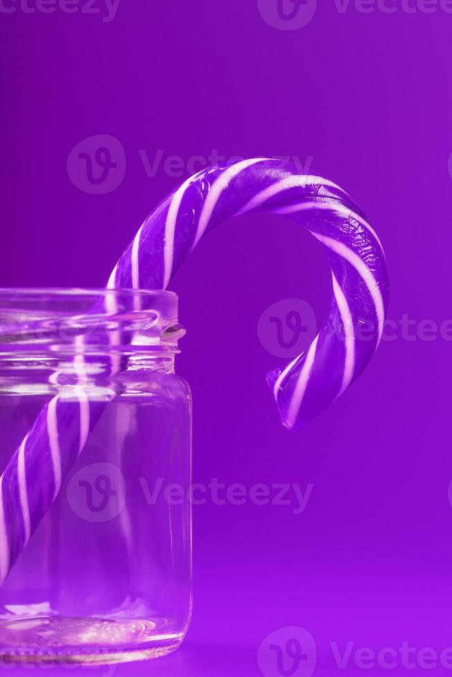 eine Lutscher-Zuckerstange in einem Glas auf violettem Hintergrund. foto