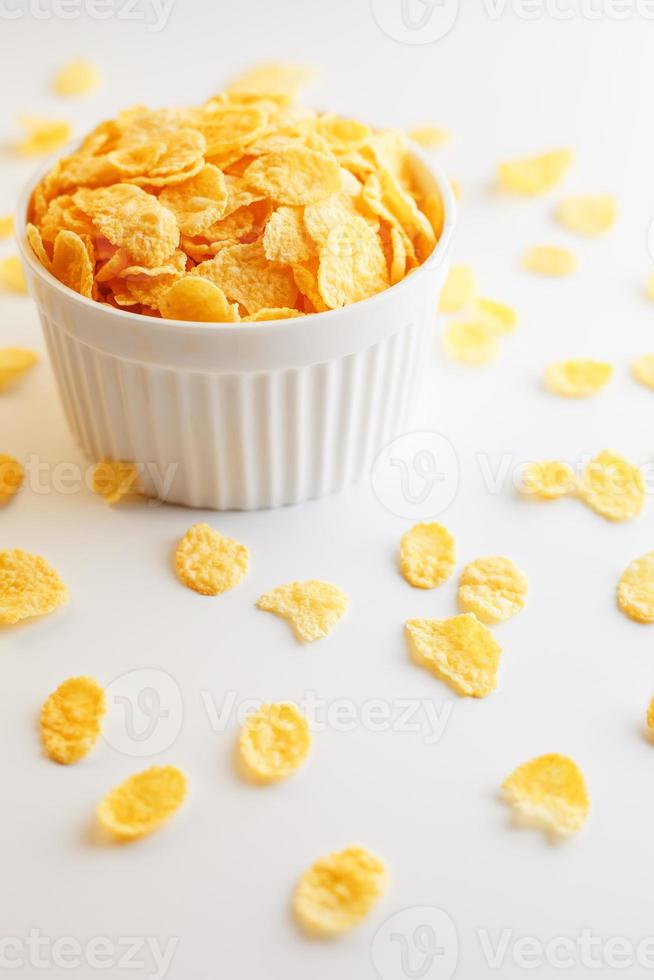 weiße Tasse mit goldenen Cornflakes, isoliert auf weißem Hintergrund. Hopya zerbröckelte um die Tasse herum. Sicht von oben. leckeres und gesundes Frühstück foto