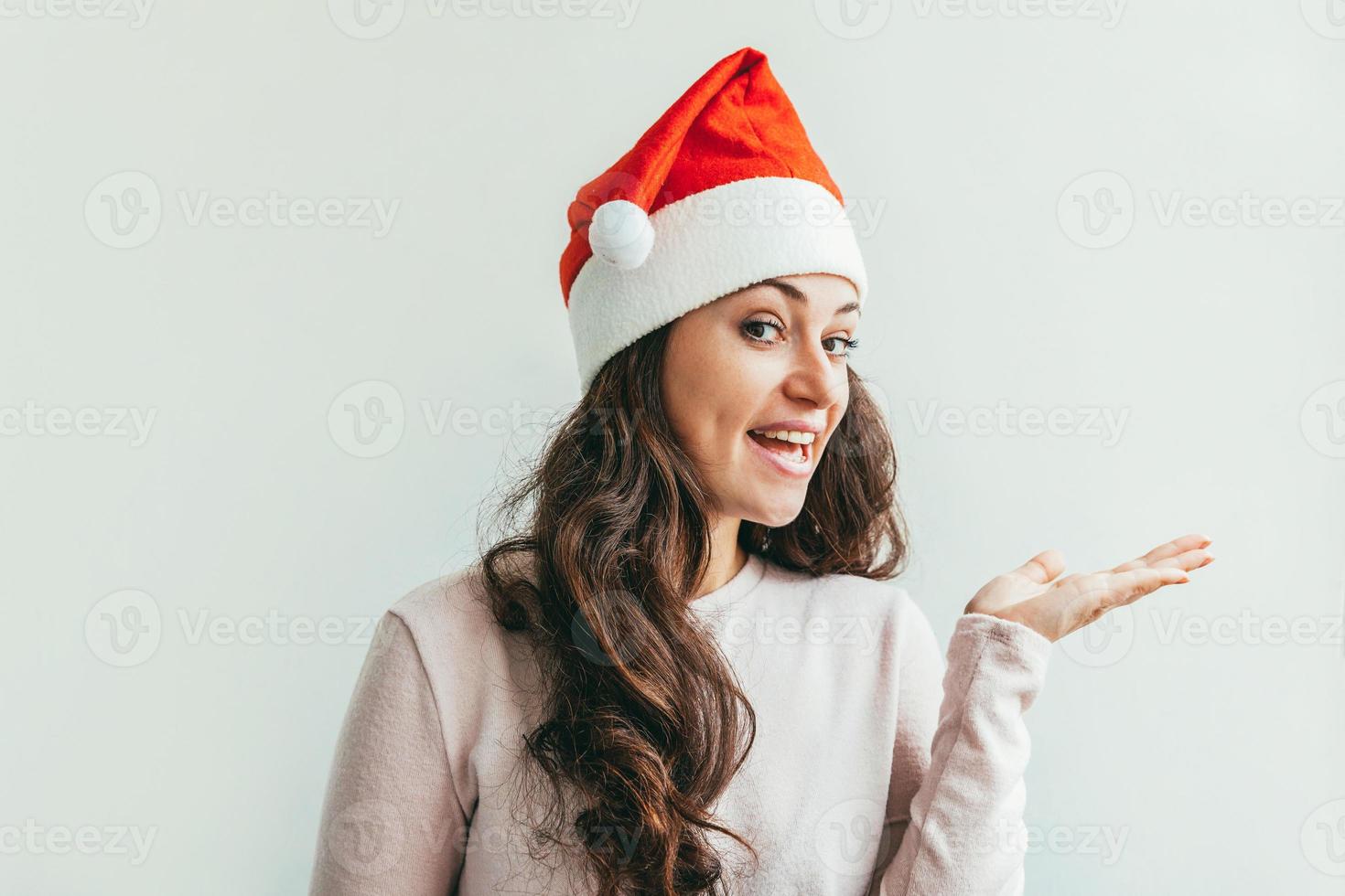 Schönes Mädchen in rotem Weihnachtsmann-Hut, das offene Palmenhand auf weißem Hintergrund zeigt foto