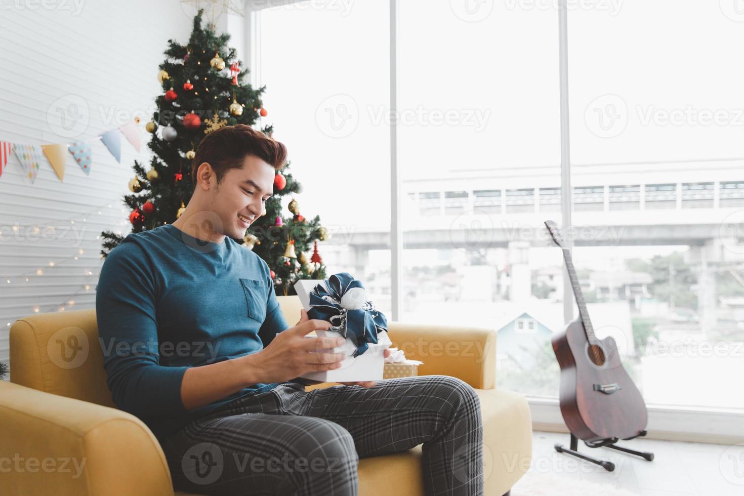 lächelnder hübscher junger mann, der zu hause weiße weihnachtsgeschenkbox öffnet foto