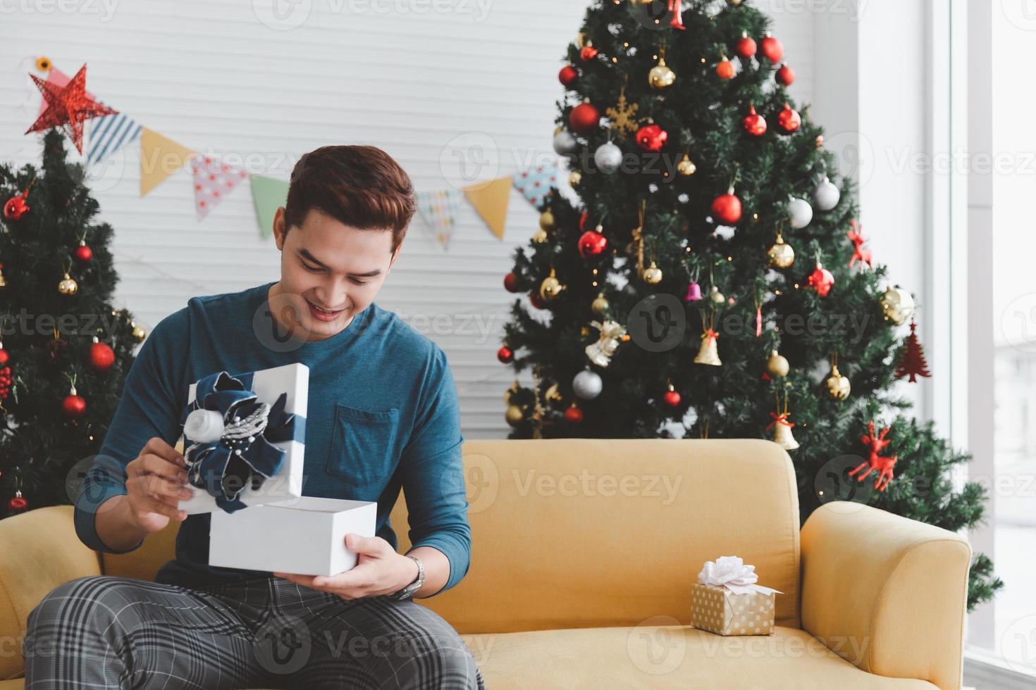 lächelnder hübscher junger mann, der zu hause weiße weihnachtsgeschenkbox öffnet foto