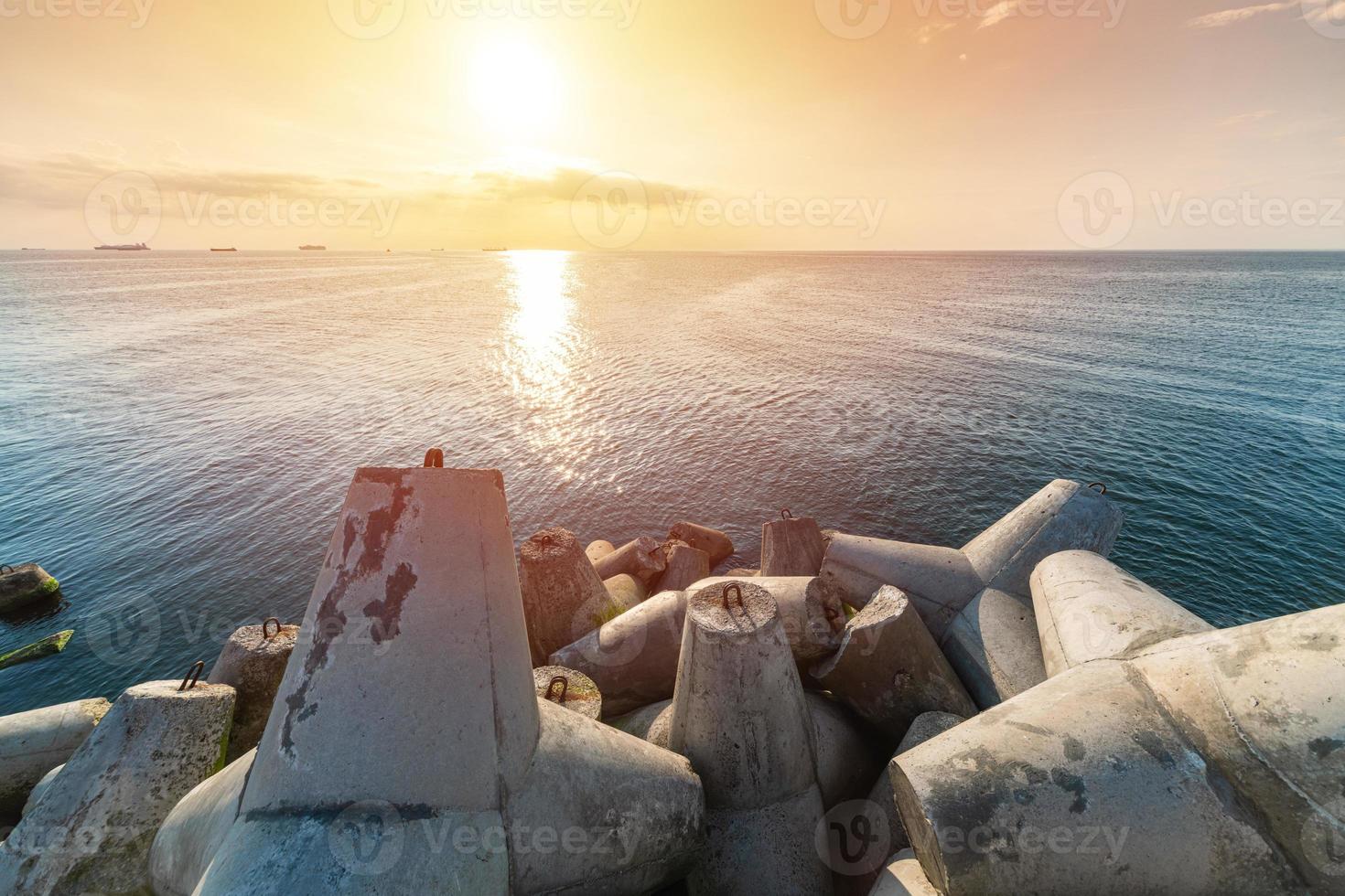 schöne sonnenuntergang seelandschaft. Reiseträume und Motivation. Wellenbrecher Tetrapoden am Ufer des Piers. Frachtschiffe am Horizont. foto