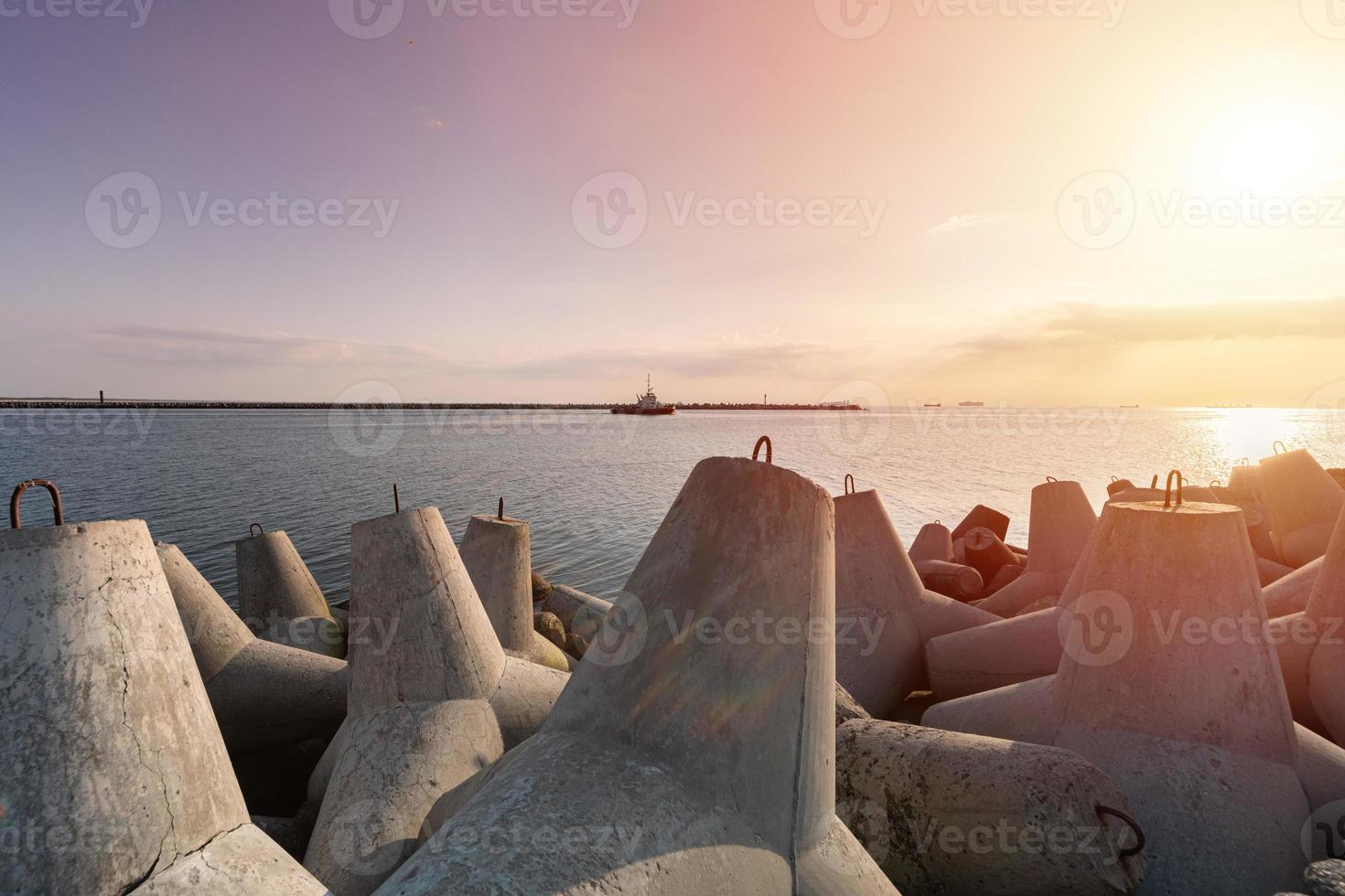 Schiffsschlepper fährt auf hoher See, um ein Frachtschiff in den Hafen zu schleppen. schöner Sonnenuntergang über dem Pier. Tetrapoden-Wellenbrecher im Hafen. foto