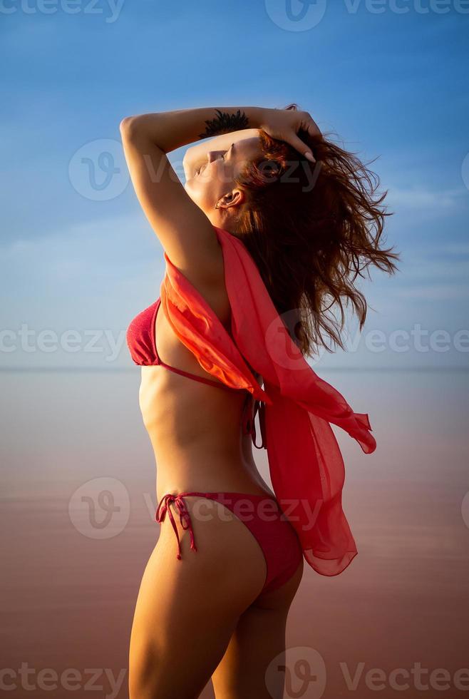 Silhouette eines Mädchens in einem roten Badeanzug am Strand. rotes Gewebe entwickelt sich in ihren Händen. foto