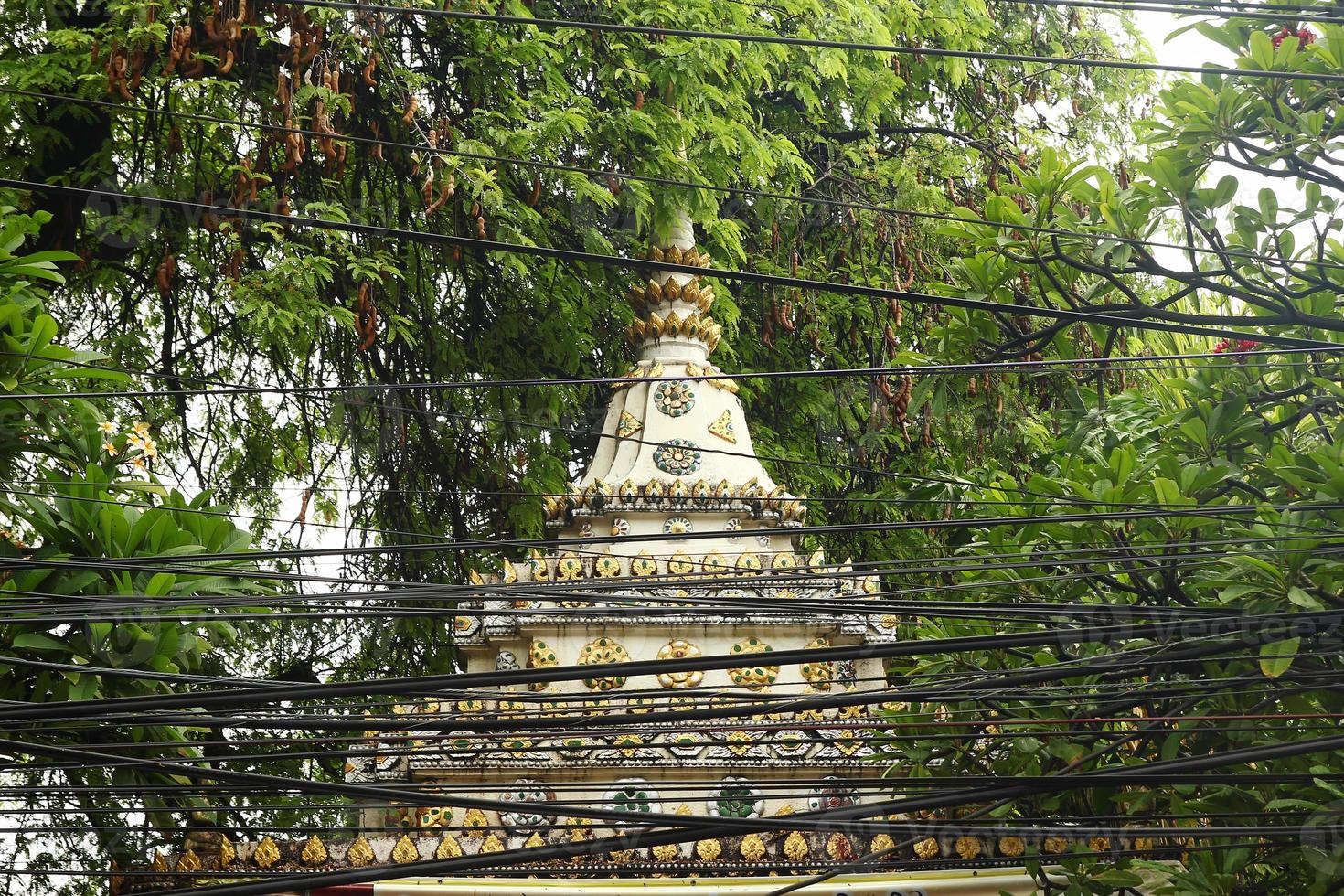 Blick auf einen buddhistischen Tempel zwischen Bäumen mit elektrischen Drähten im Vordergrund. Chiang Mai, Thailand. foto