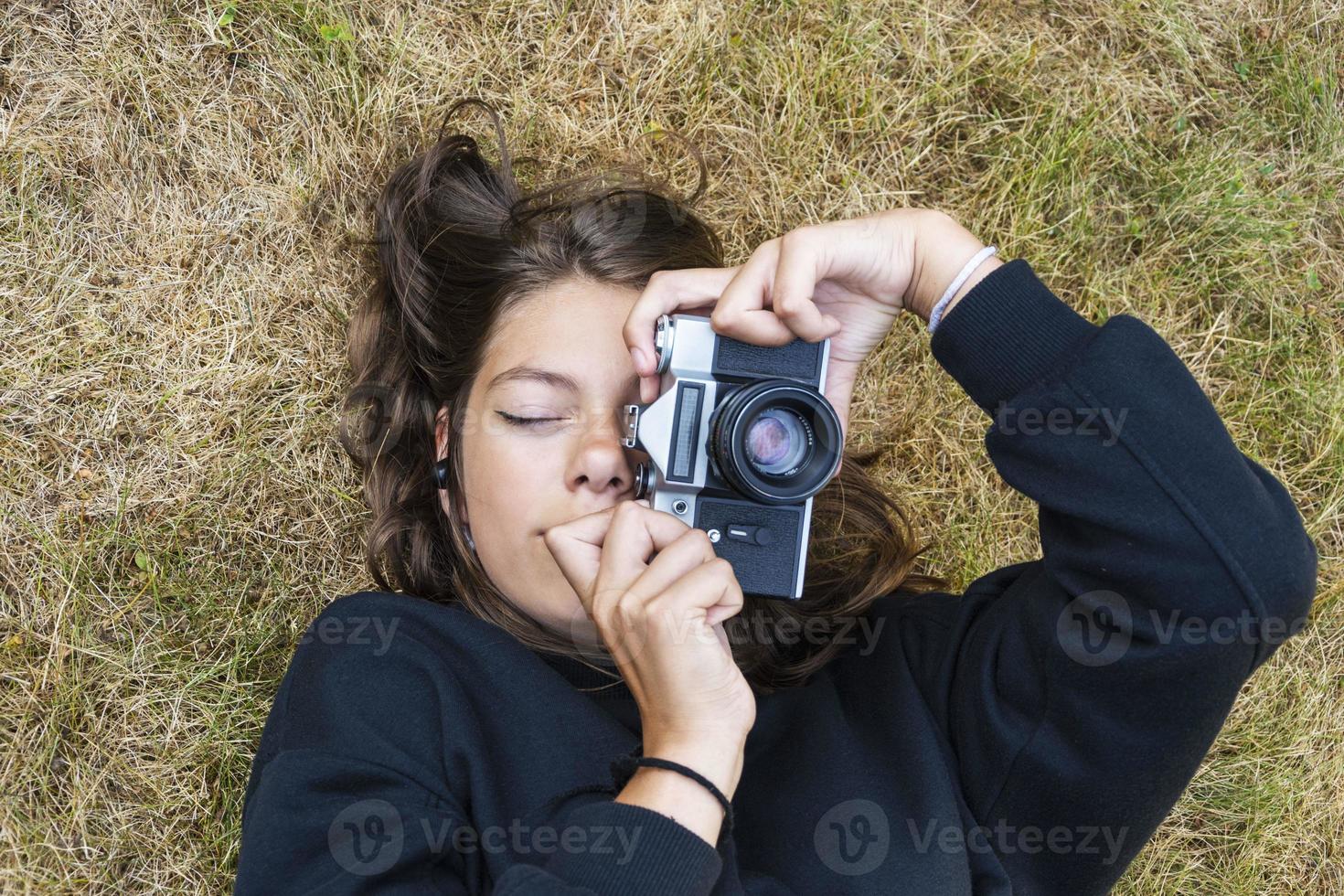 süßes jugendlich Mädchen mit einer Kamera, ein Mädchen, das Fotos auf einer Retro-Vintage-Kamera auf dem Gras im Park macht, ein Hobbykonzept