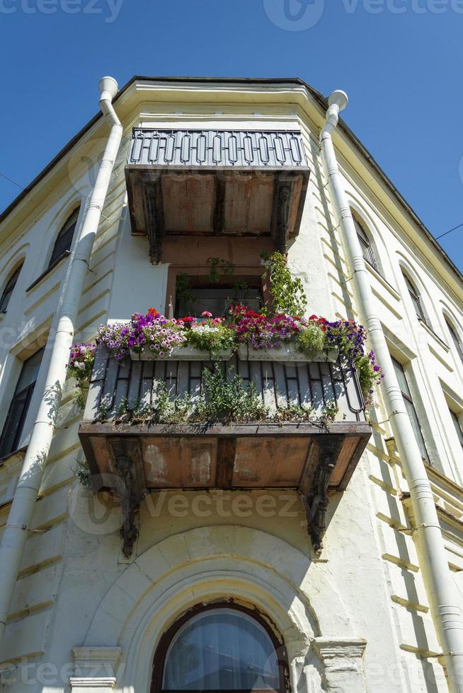 Sonnige Fassade eines alten Stadthauses, traditioneller europäischer Balkon mit hellen Blumen und Blumentöpfen, Fenster foto
