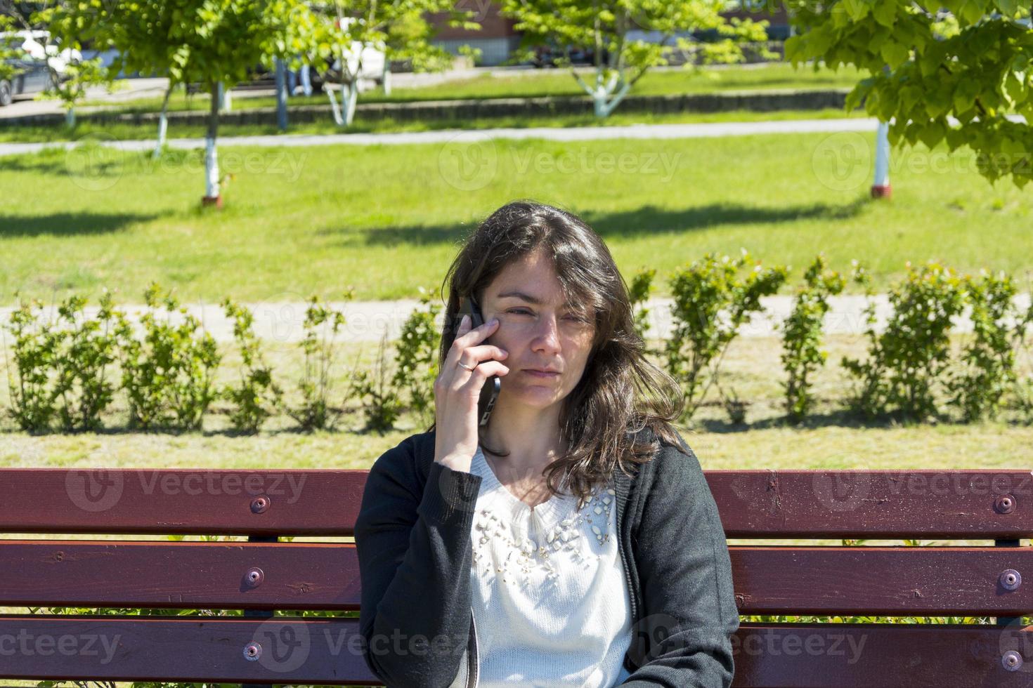 süßes kaukasisches mädchen mit einem telefon auf einer parkbank im sommer foto