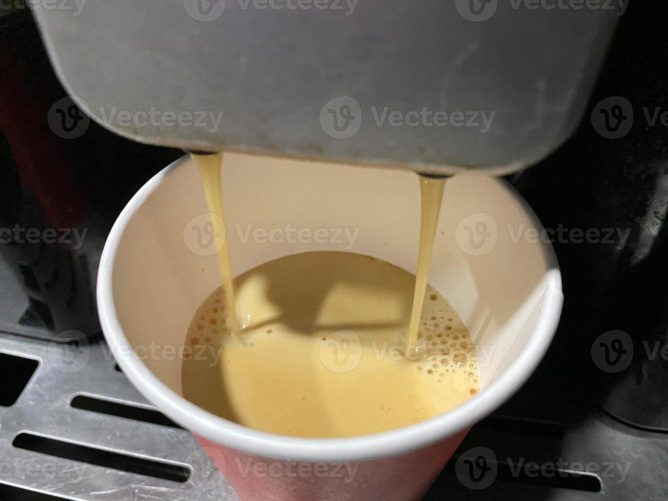 rote kaffeetasse aus pappkarton, in die morgens im büro köstlicher belebend heißer schwarzer americano-kaffee aus der kaffeemaschine gegossen wird foto