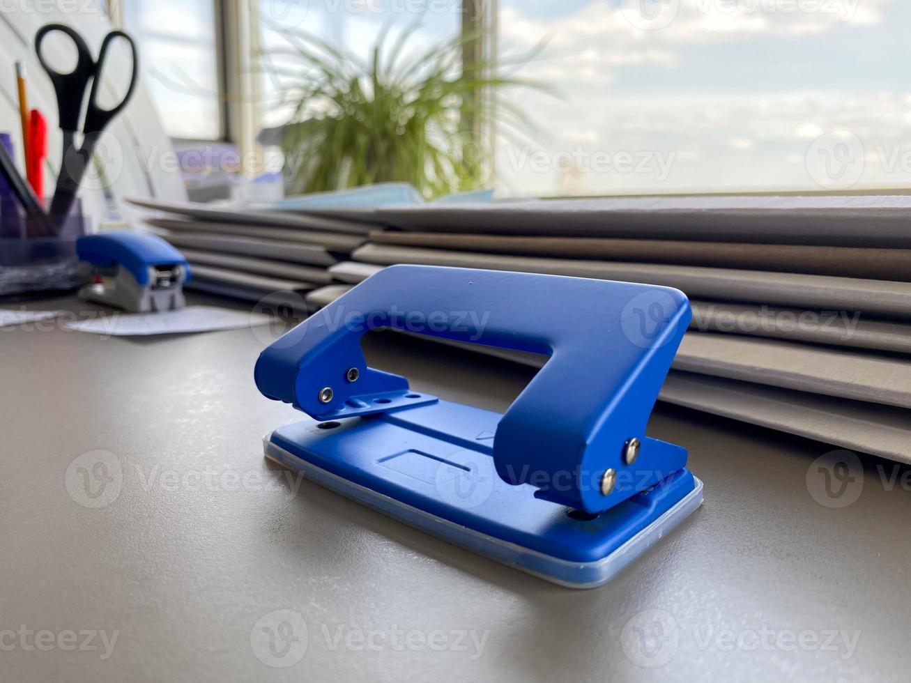 Bürolocher aus blauem Eisenmetall zum Lochen von Papierbögen und Dokumenten auf dem Arbeitstisch im Büro. Schreibwaren foto