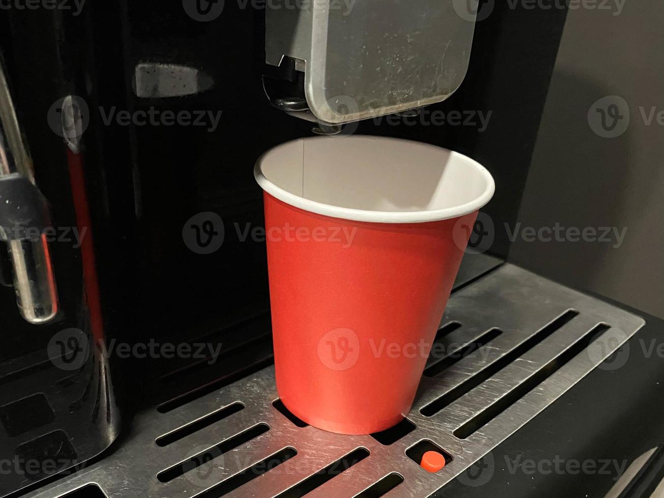 rote kaffeetasse aus pappkarton, in die morgens im büro köstlicher belebend heißer schwarzer americano-kaffee aus der kaffeemaschine gegossen wird foto