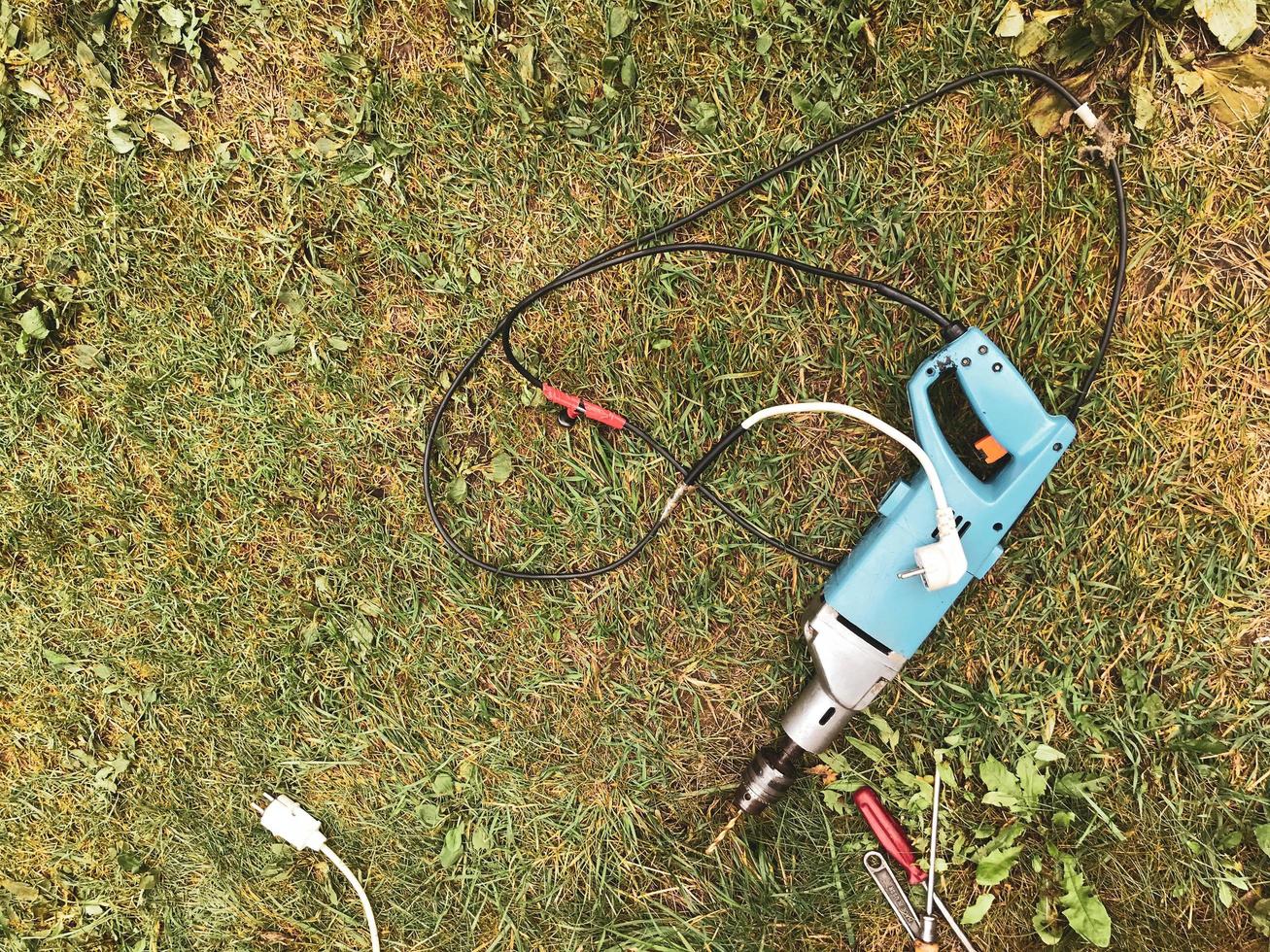 Auf dem Gras liegt ein Bohrer mit einem langen Bohrer im Inneren. Renovierung in der Natur. neben einem Schraubendreher mit rotem Griff. Reparatur eines Holzhauses und Daches. Werkzeuge für die Reparatur. Hausbau foto