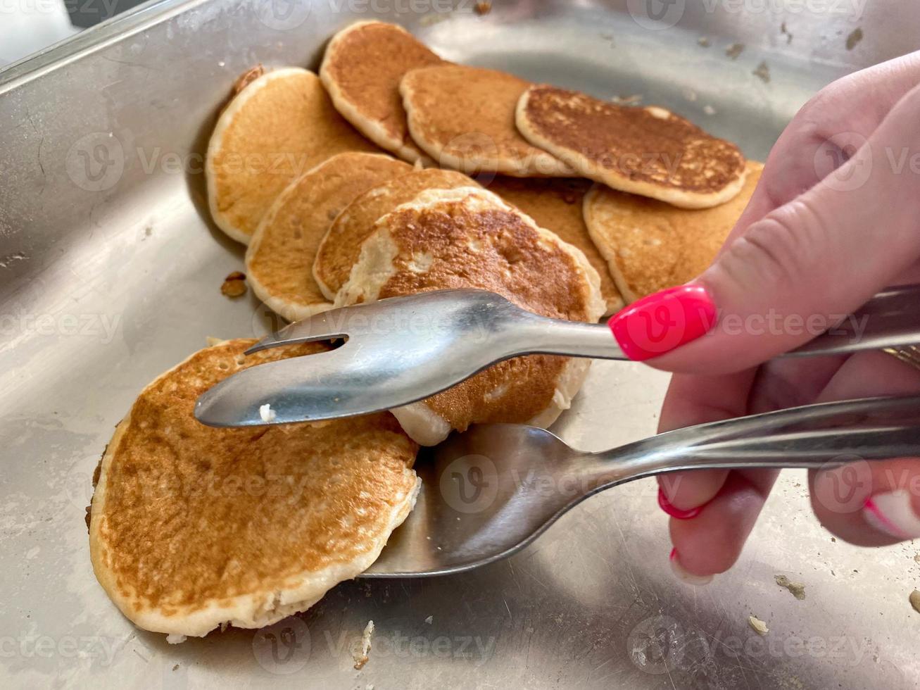 Eine schöne Hand eines Mädchens nimmt mit einer Zange köstliche Mehlpfannkuchen zum Frühstück von einem Teller in einem Kantinencafé. der Hintergrund. Textur foto