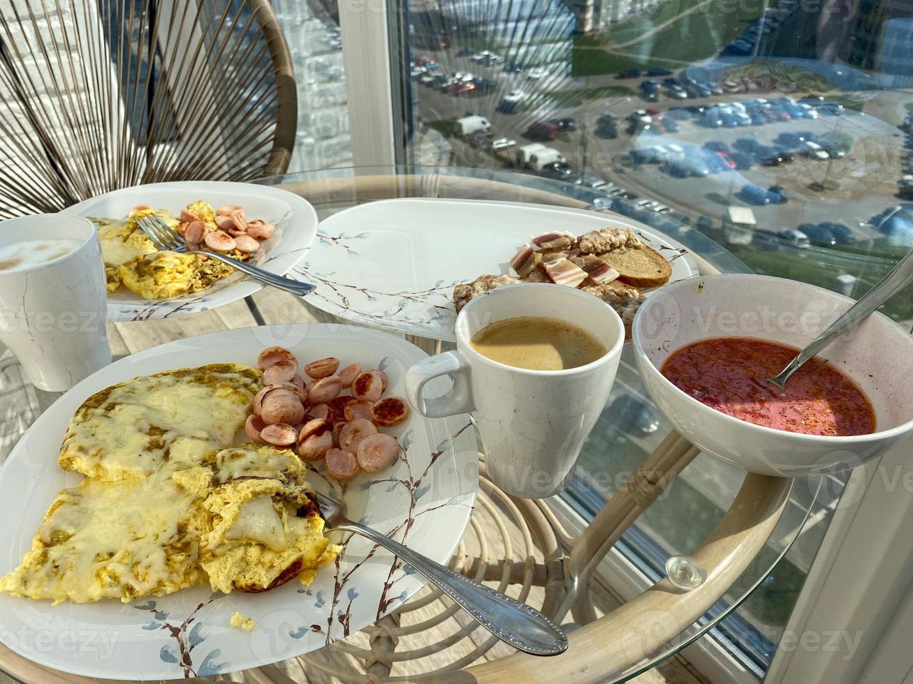 Ein schönes, herzhaftes und gesundes Frühstück am Morgen mit Eieromelett, Kaffee und Sandwiches auf Tellern und Tassen auf einem Glastisch foto