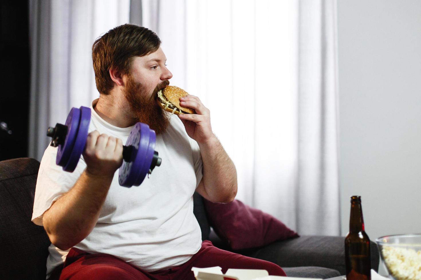 Mann, der einen Hamburger isst, während er Gewichte hebt foto