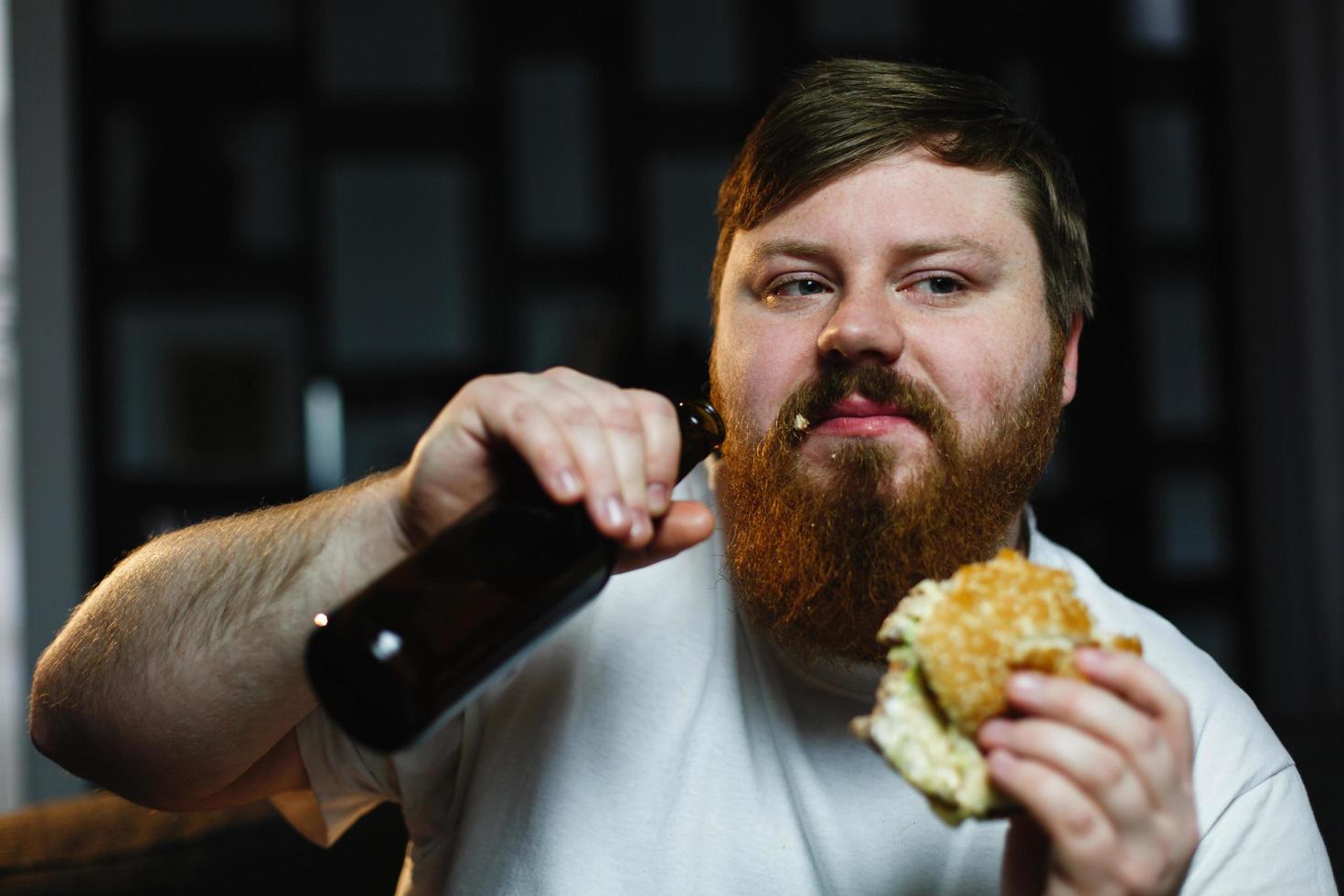 dicker Mann sieht fern, isst Burger und trinkt Bier foto