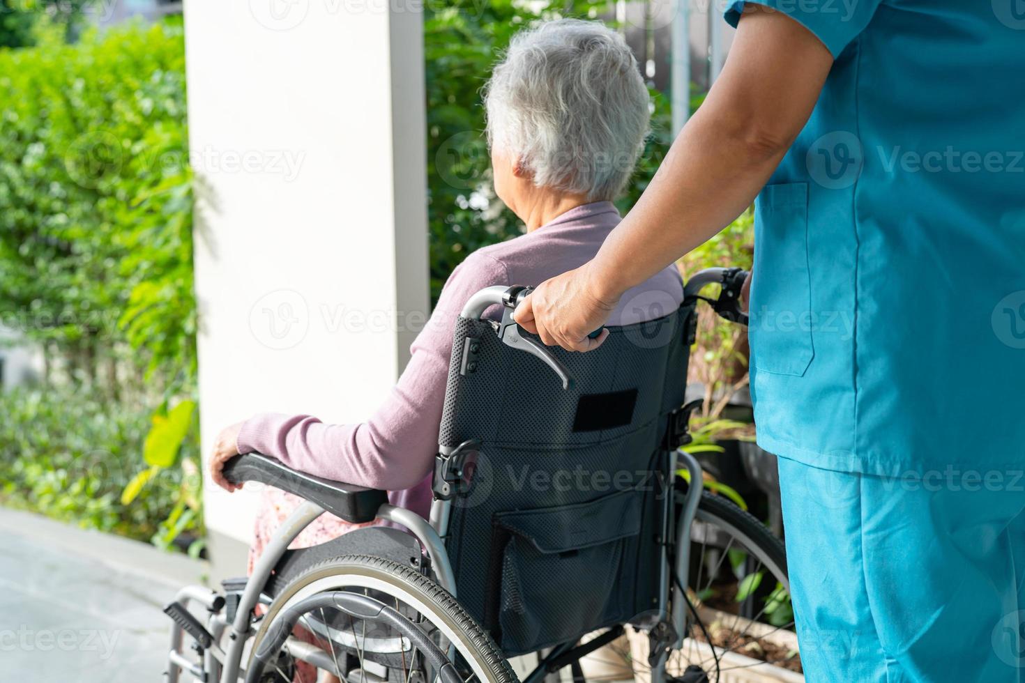 Pflegekraft hilft und pflegt asiatische Senioren oder ältere Frauen, die im Rollstuhl auf der Rampe im Pflegekrankenhaus sitzen, gesundes, starkes medizinisches Konzept foto