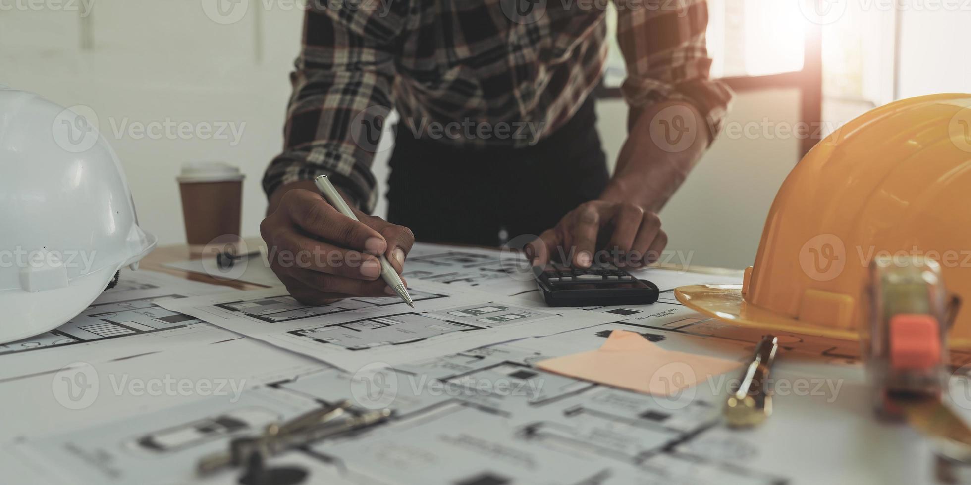 Bild eines Ingenieurs, der ein Gebäude oder Haus mit Blaupausendesign zeichnet, ein Ingenieurarbeitsplatz mit Blaupausen, Bleistift, Winkelmesser und Schutzhelm, Industriekonzept foto