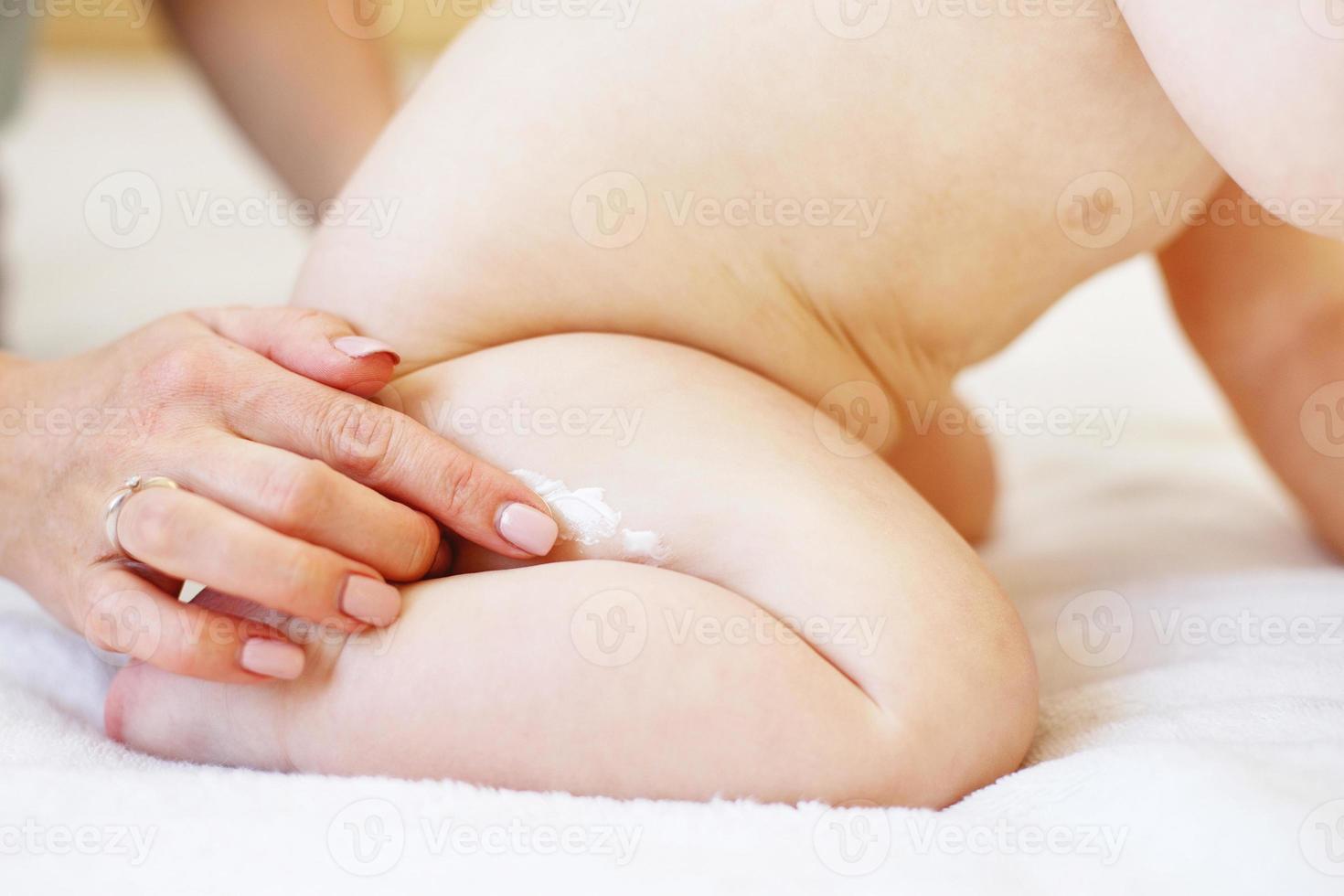 mutter, die zur hautpflege etwas creme mit der hand auf den babyarsch aufträgt. foto